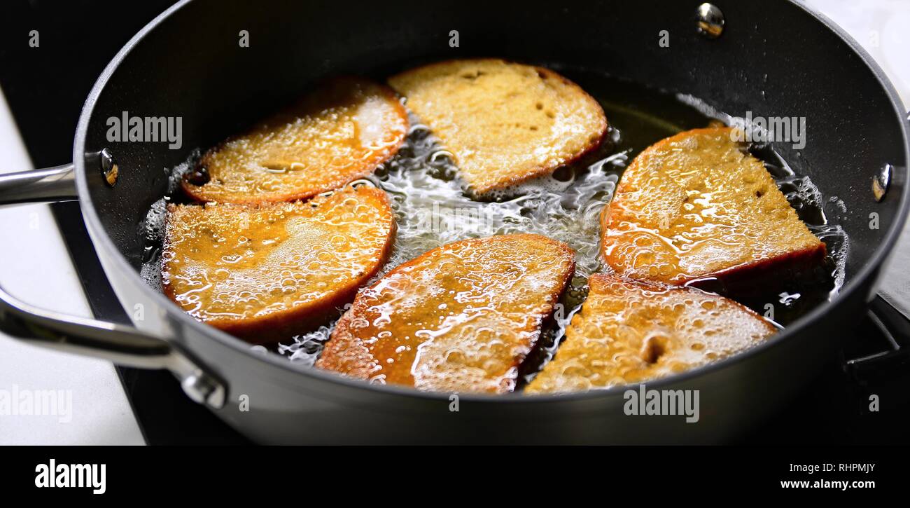 Una frittura di pane in olio caldo in padella nera vicino. Foto Stock