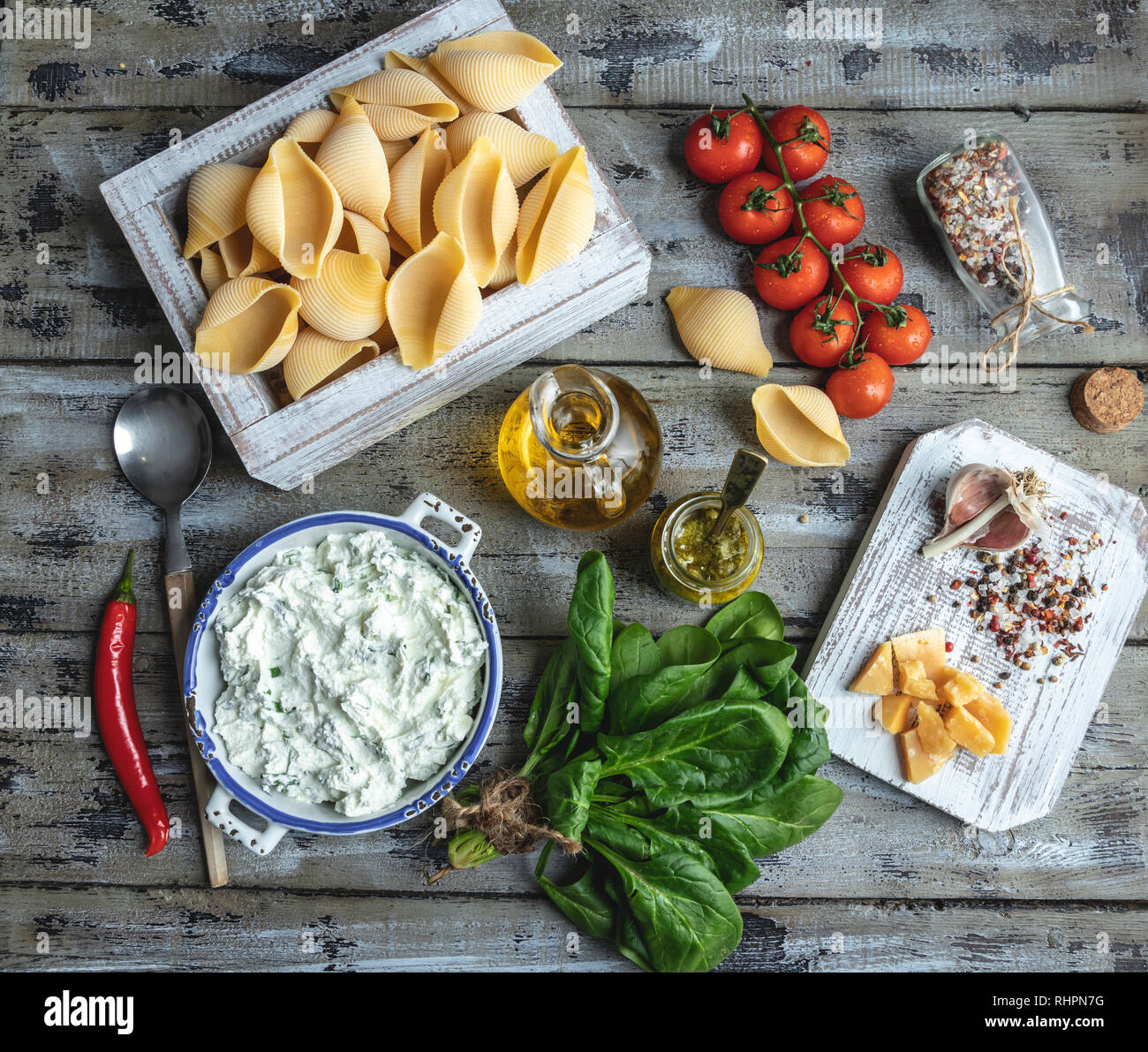 Ingredienti per la cottura della pasta. Conchiglioni, foglie di spinaci, pomodori ciliegini, parmigiano, crema di formaggio, olio d'oliva, sale, aglio, stile rustico, wo Foto Stock