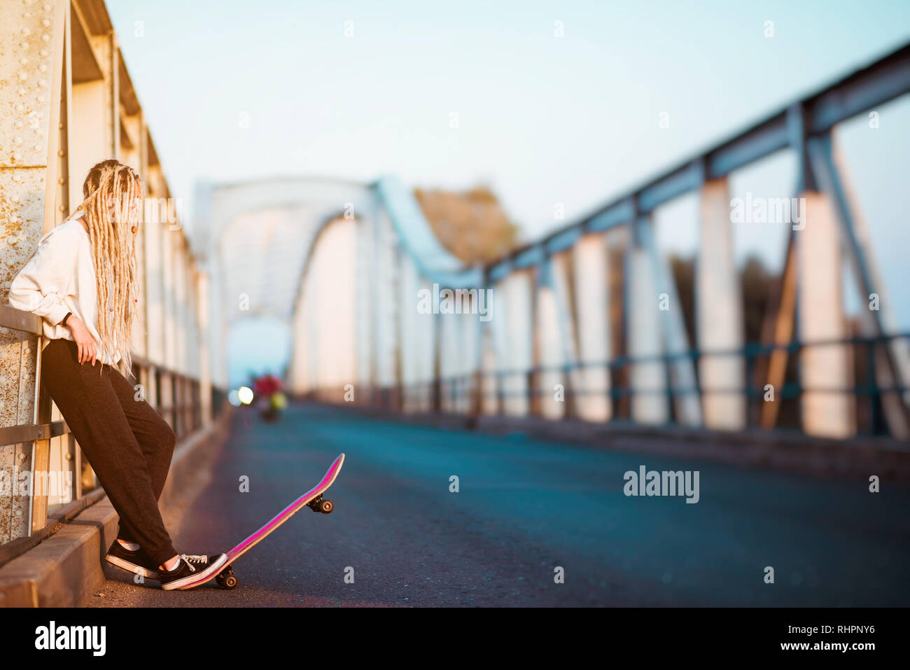 Giovane donna con lo skateboard su bridge Foto Stock