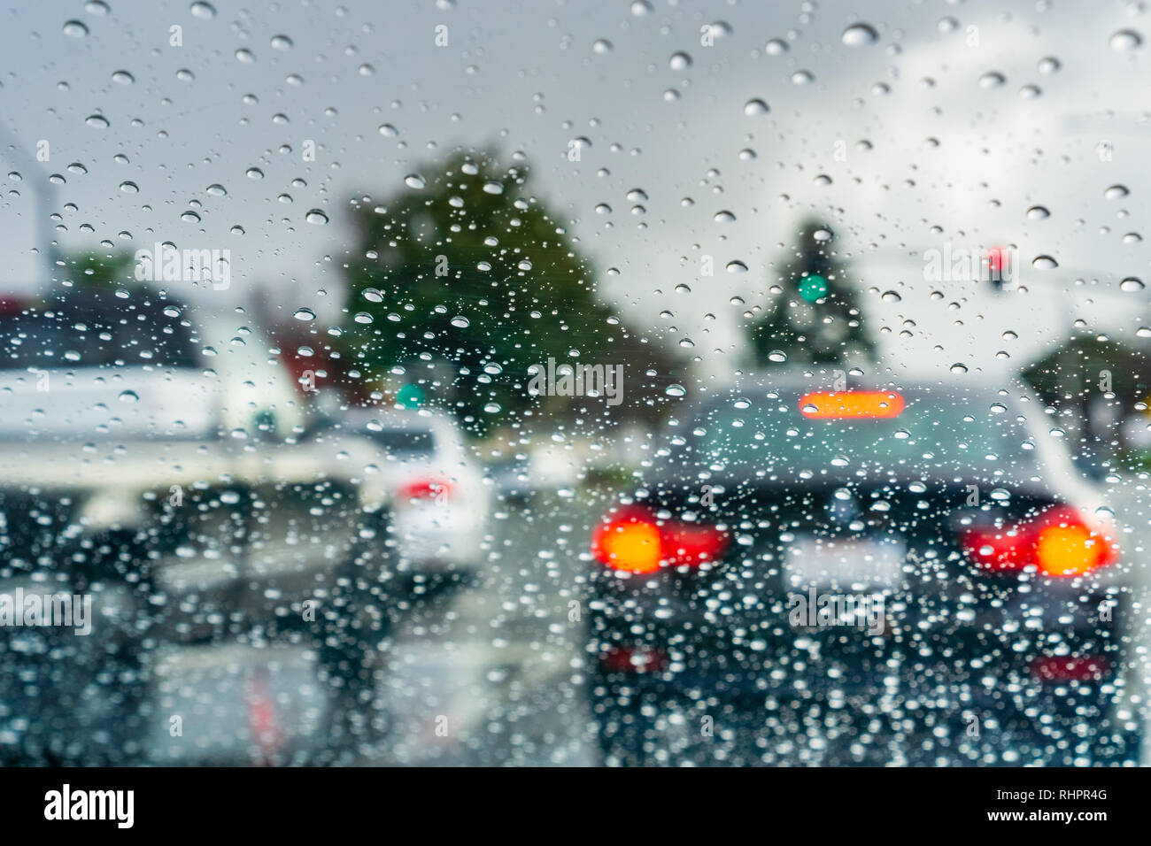 Le gocce di pioggia sul parabrezza in un giorno di pioggia; vetture fermo ad un semaforo in background; California Foto Stock