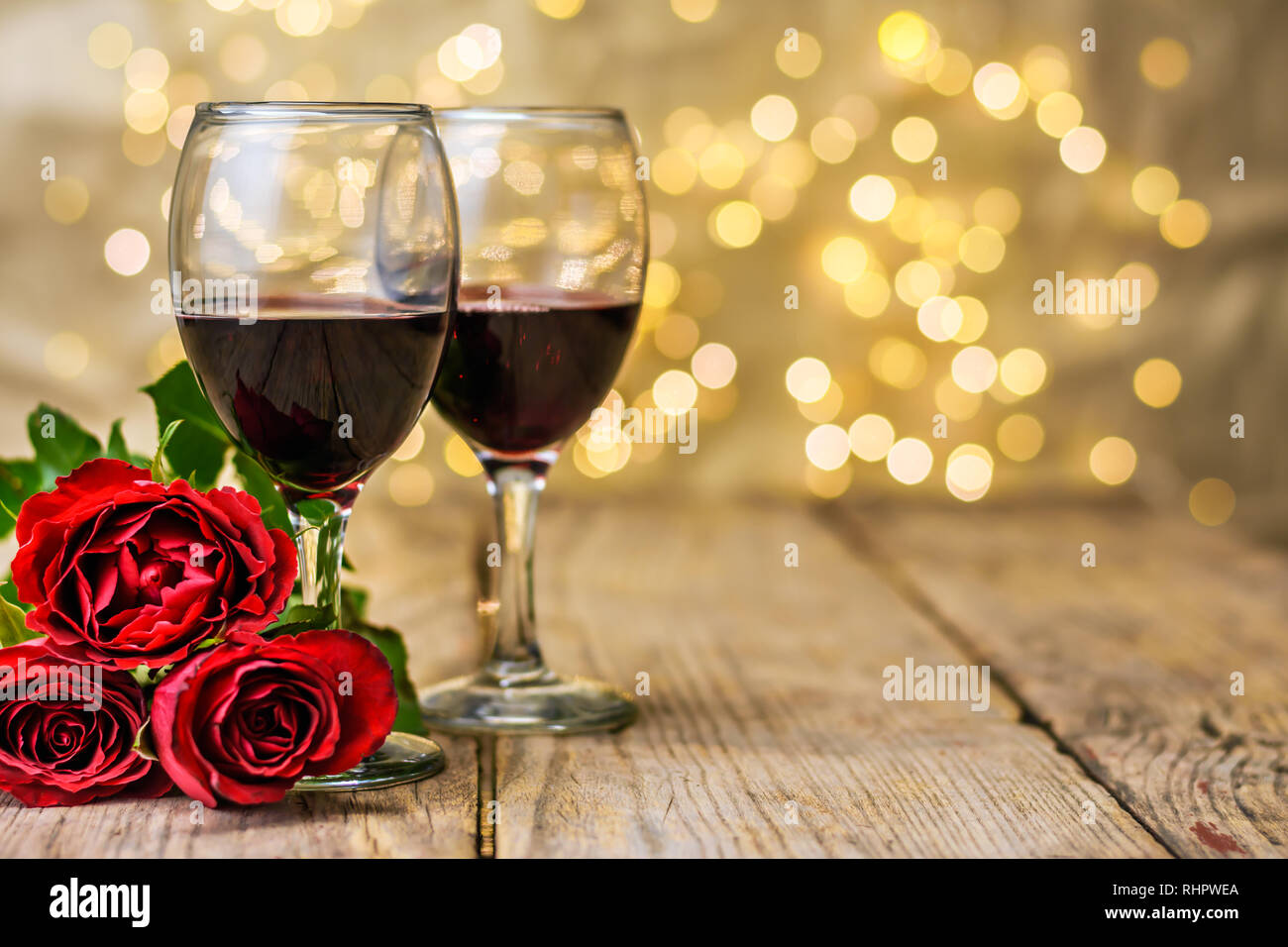 Il giorno di San Valentino ancora in vita. Due bicchieri di vino e rose rosse su una tavola in legno rustico di fronte a sfocare lo sfondo luminoso con copia spazio per t Foto Stock