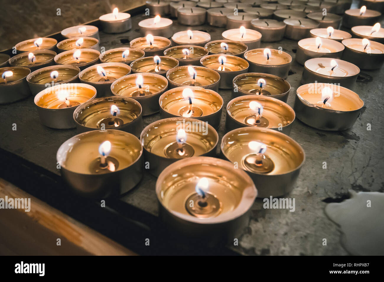 La masterizzazione memorial candele su sfondo scuro. numerose rotonde memorial candele in portacandele. Un fuoco che brucia sulle candele in piedi sulla tavola. Foto Stock