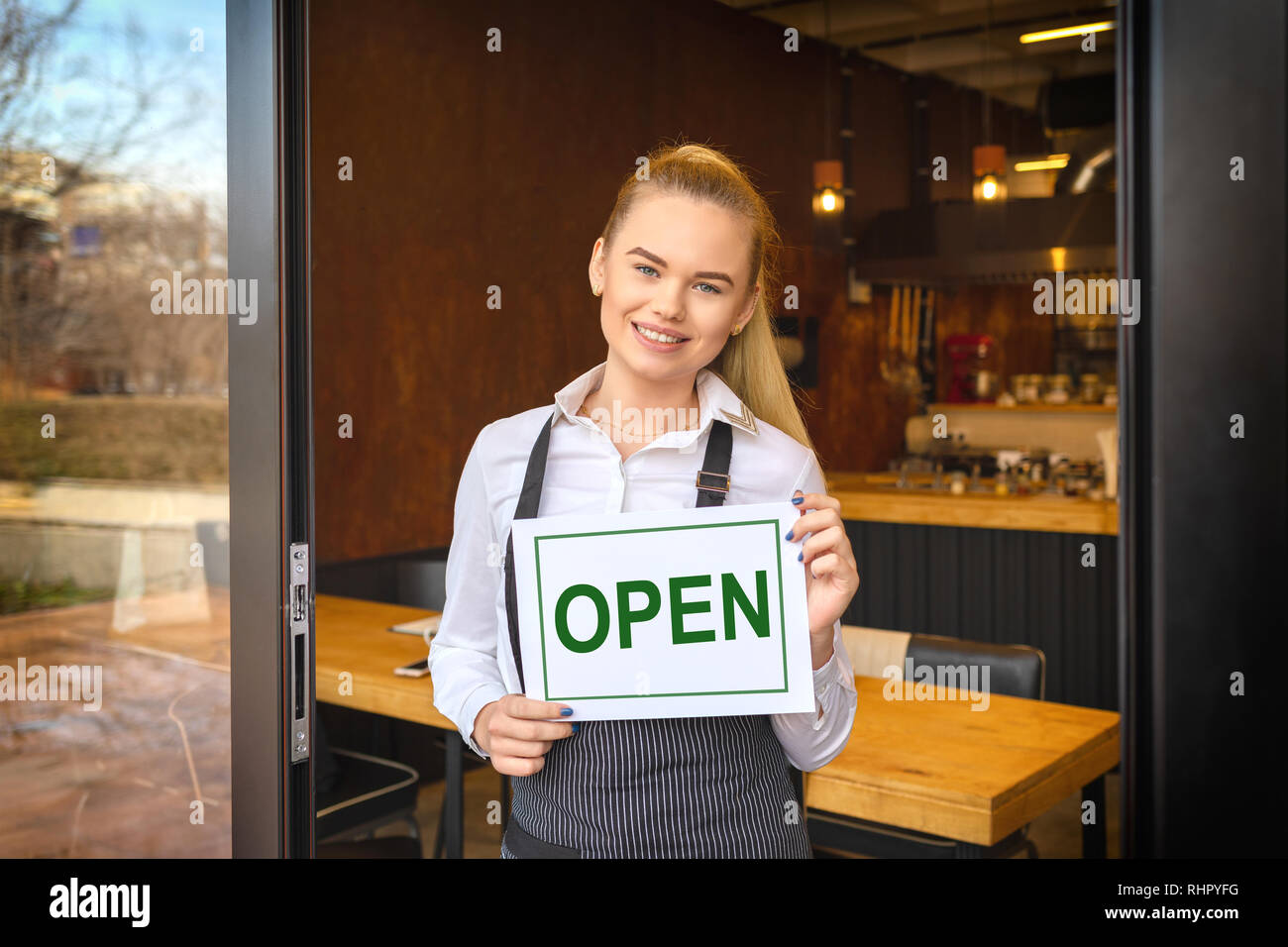 Ritratto del proprietario sorridente permanente al ristorante porta tenendo aperte segno, giovane donna imprenditore appoggiata alla porta di ingresso della nuova famiglia piccola busines Foto Stock