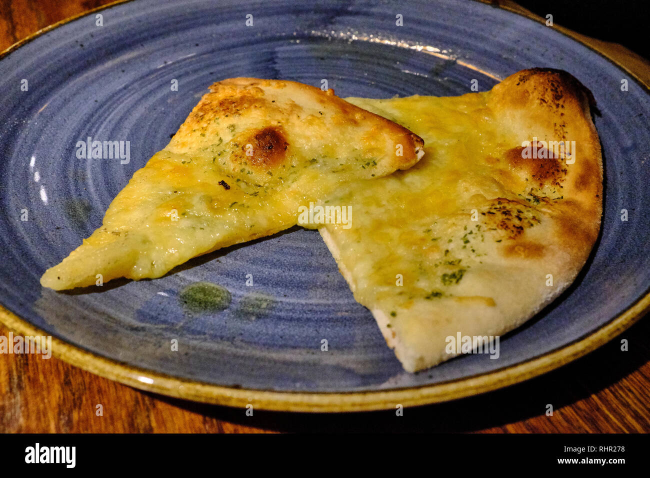 Una grande e una piccola fetta di pietra piatti cotti al forno pane con burro all'aglio insieme su una grande blu piastra colorata Foto Stock