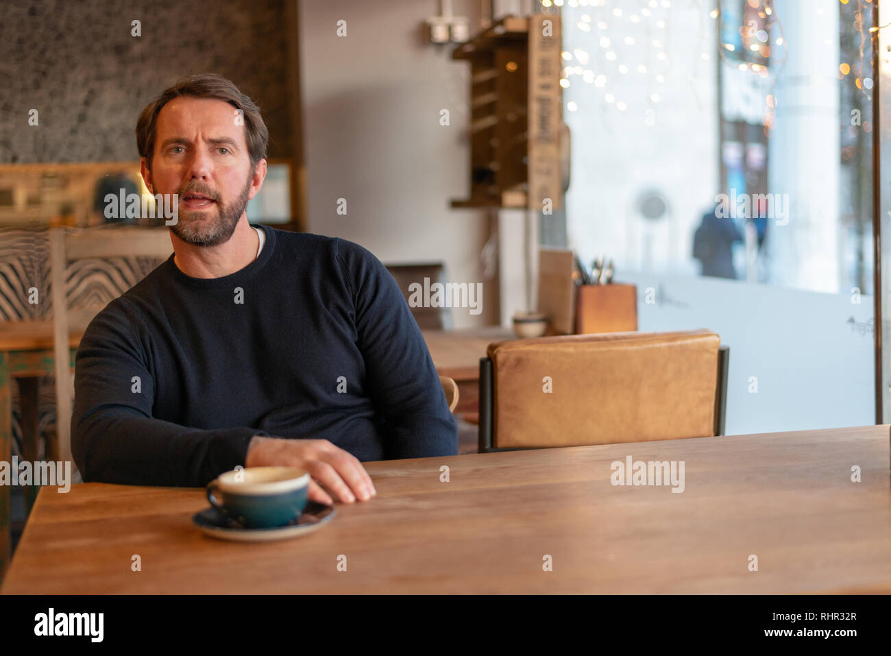 Di mezza età maschio caucasico seduti a tavola in un coffee shop che esprimono incredulità e antipatia Foto Stock