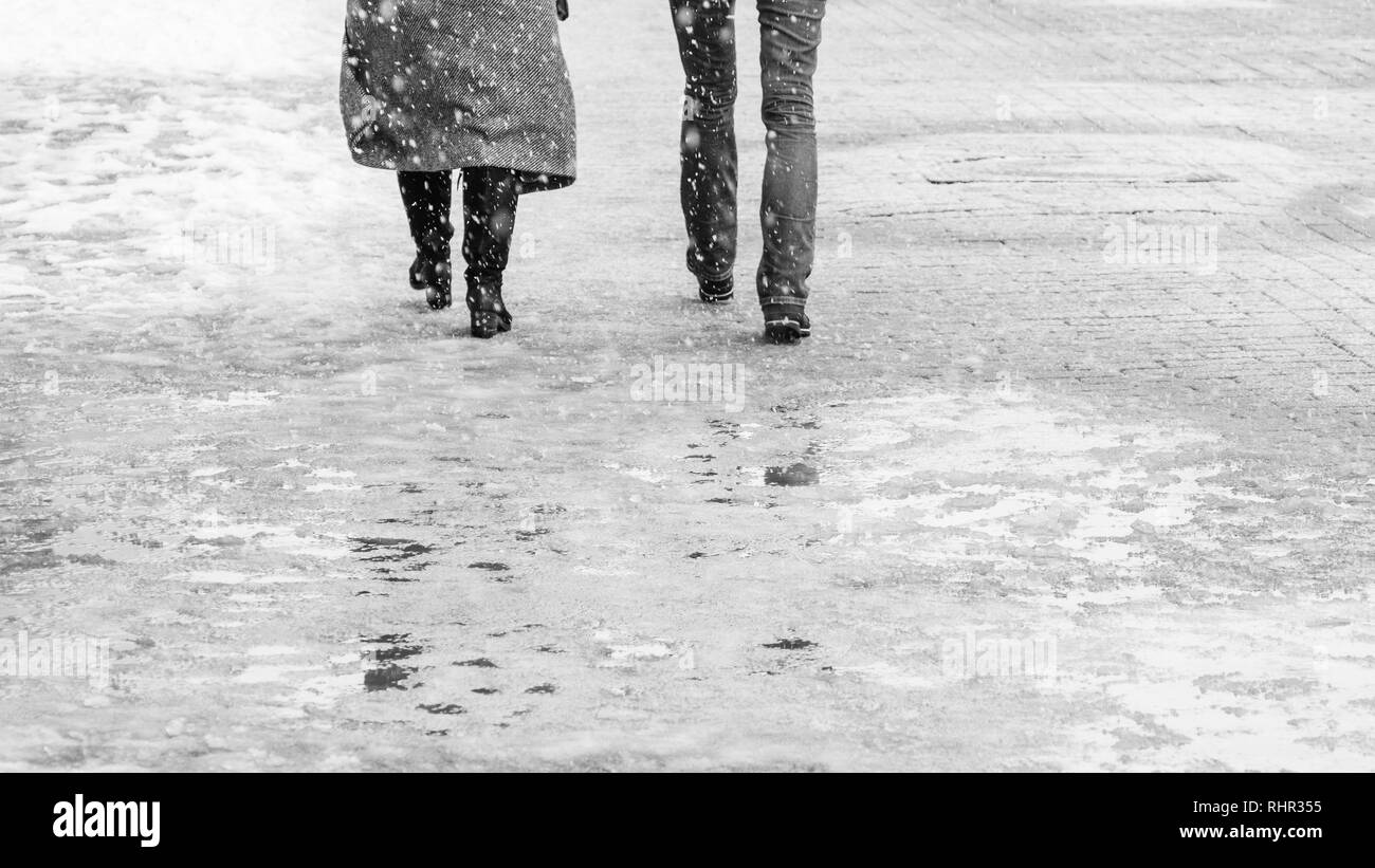 Winter City marciapiede scivoloso. Vista posteriore sui piedi della gente che cammina lungo la ghiacciate nevoso marciapiede. Coppia di scarpa sulla strada ghiacciata in inverno. Abstract rilevare Foto Stock