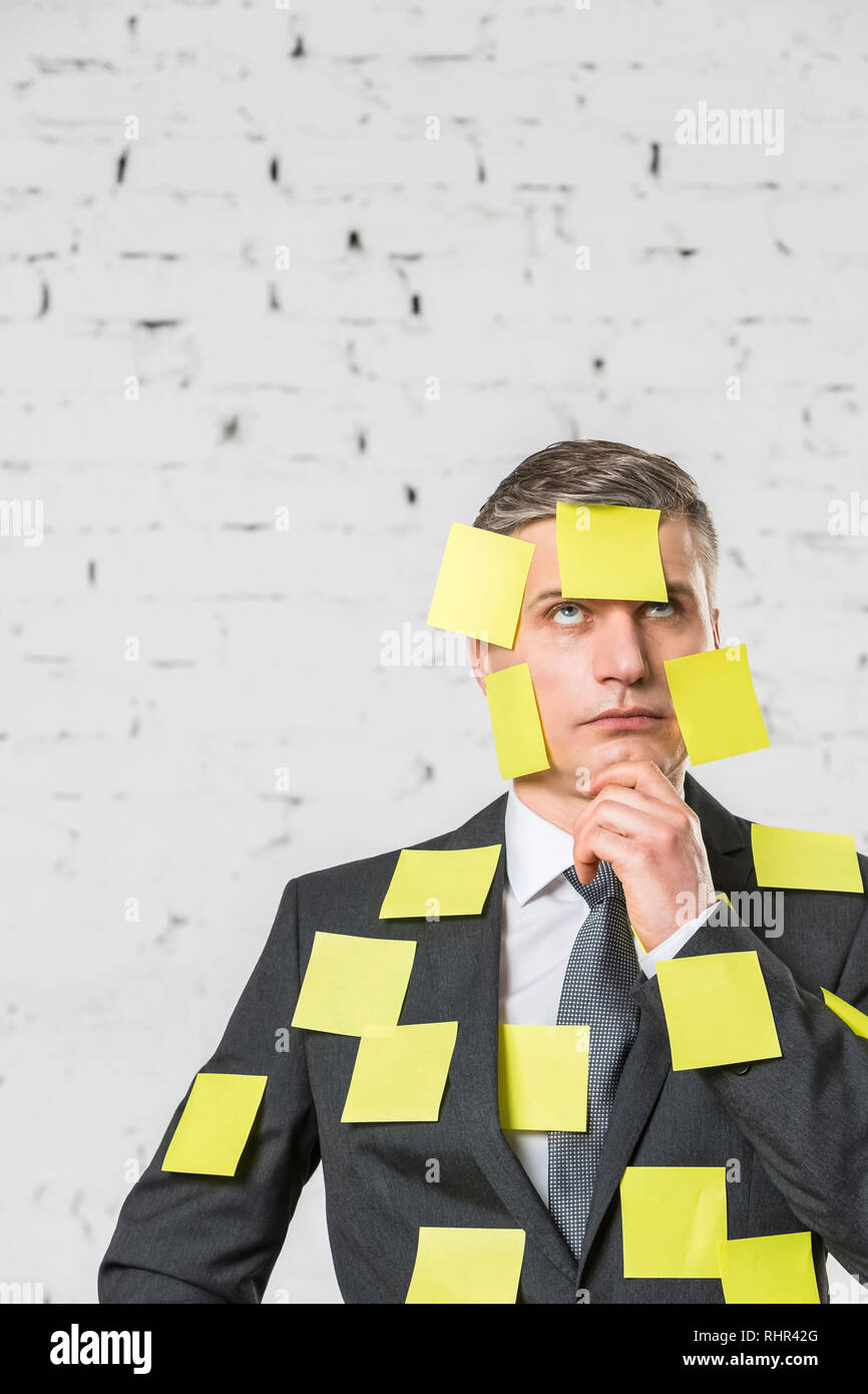 Considerato maturo imprenditore con giallo vuota note adesive sulla faccia e tuta contro la parete in ufficio Foto Stock
