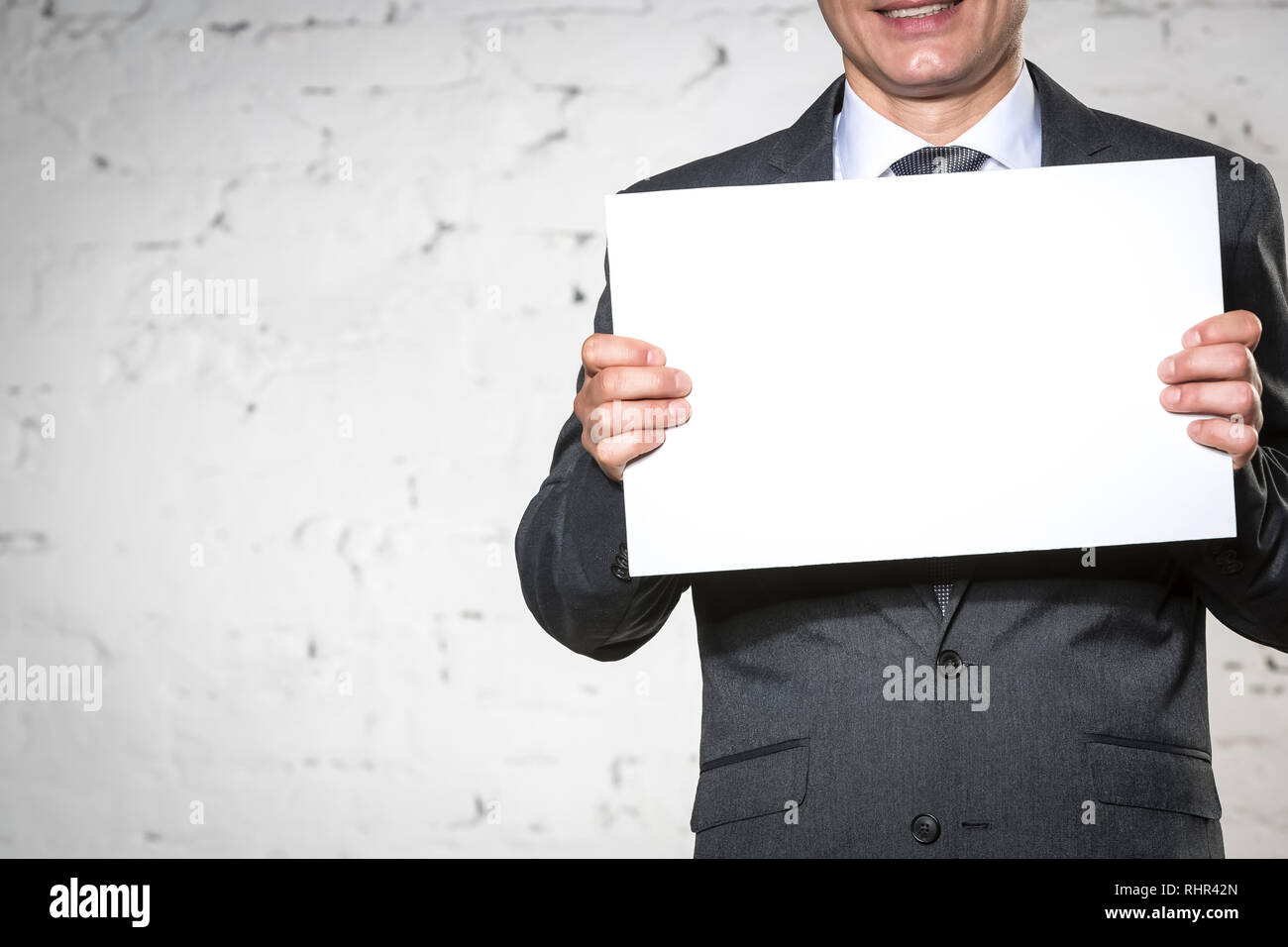 Sezione mediana di imprenditore sorridente holding targhetta vuota mentre in piedi contro il bianco muro di mattoni Foto Stock