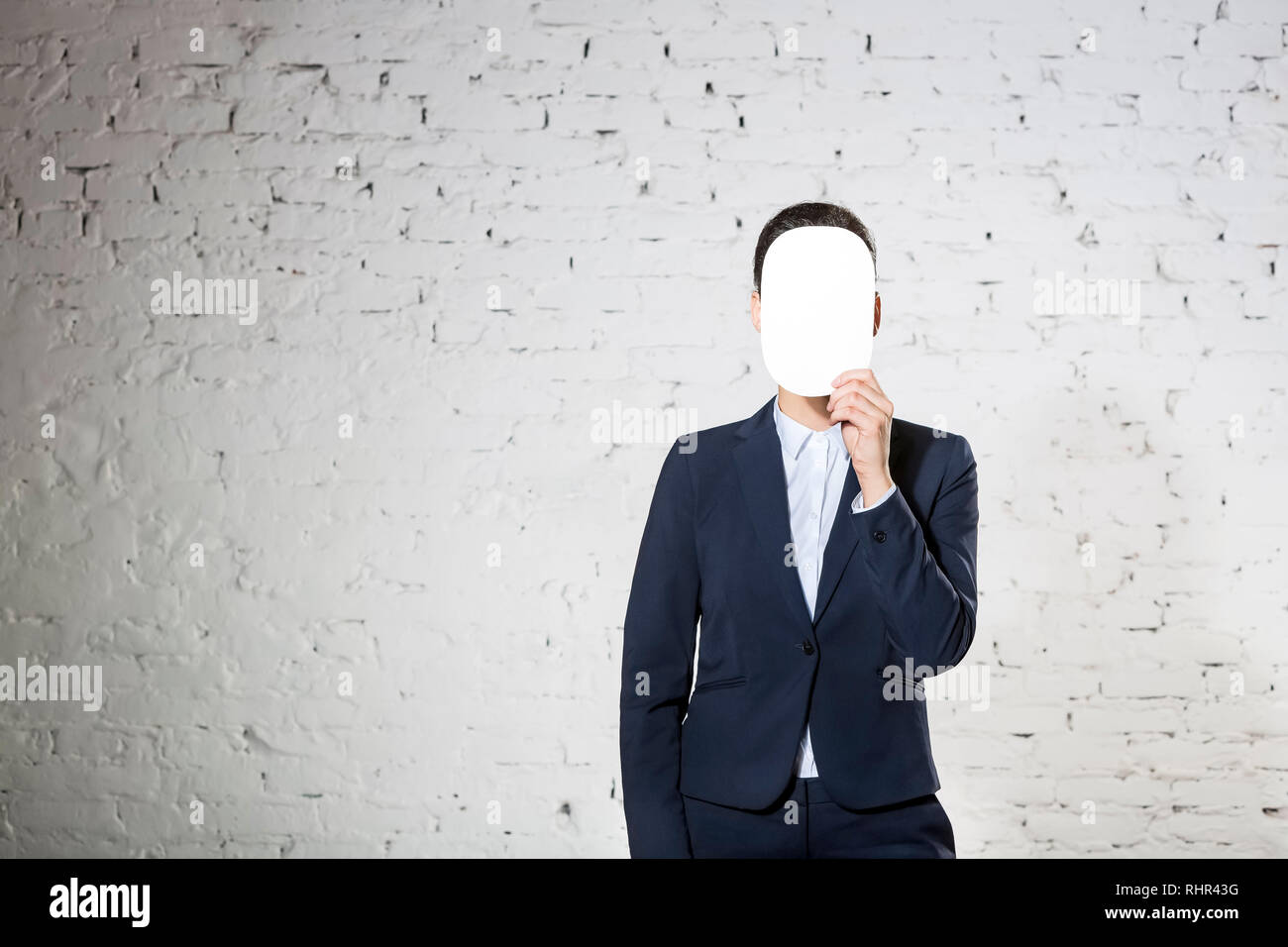 Giovane imprenditrice che ricopre la faccia con fogli di carta bianca bianco contro un muro di mattoni in ufficio Foto Stock