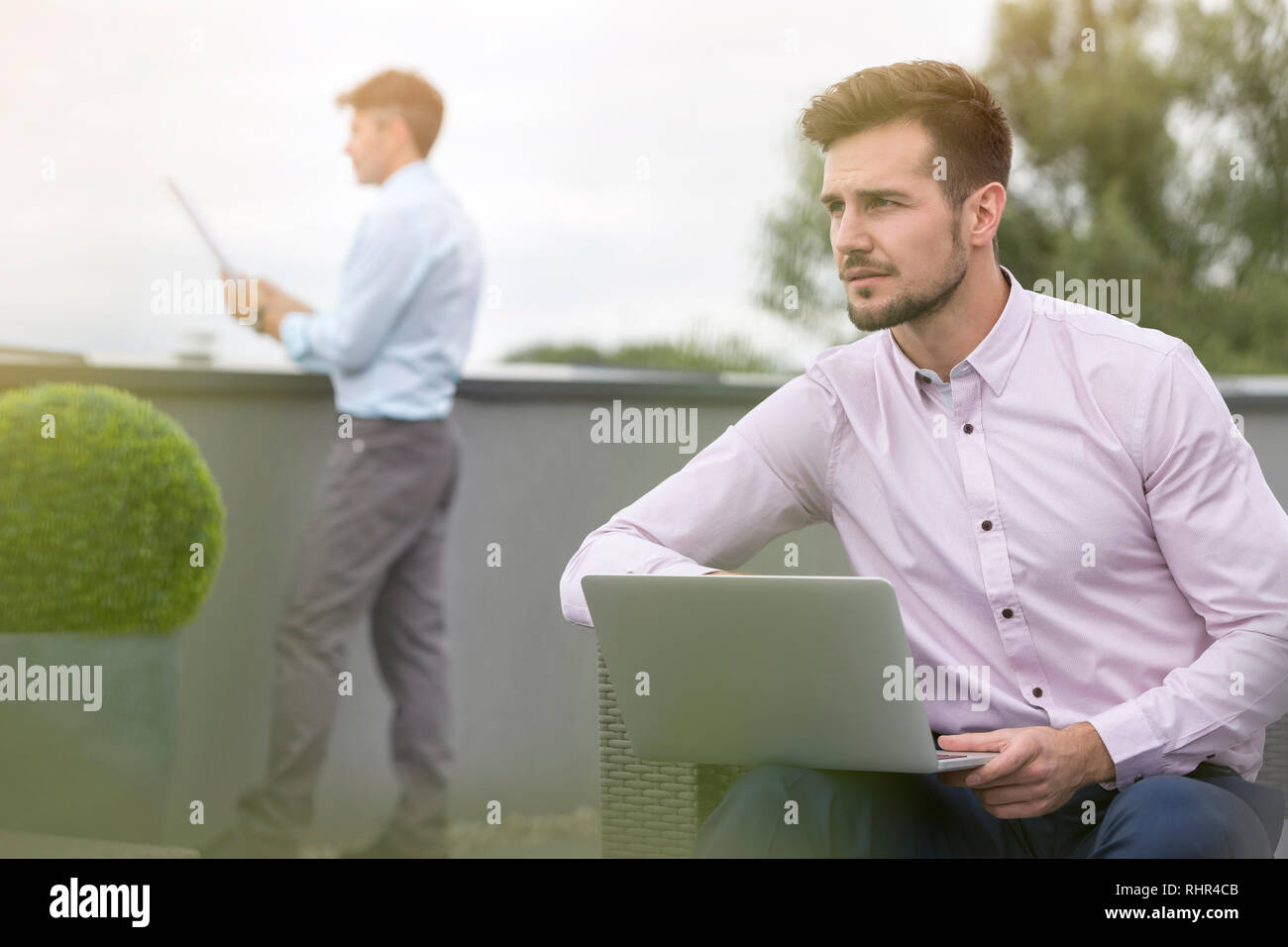 Uomo d affari con computer portatile con il collega in background in terrazza per ufficio Foto Stock