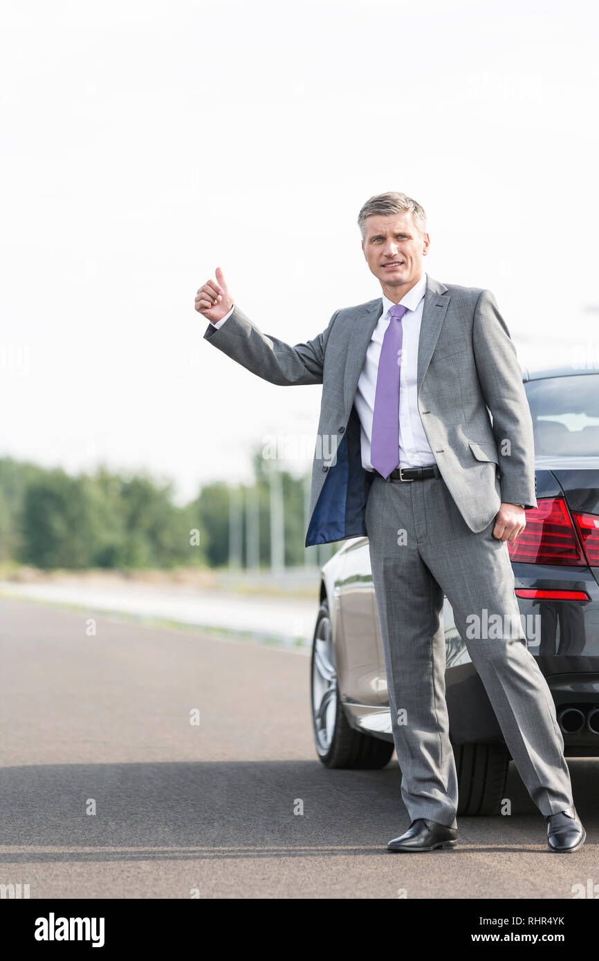 Imprenditore autostop mentre in piedi dalla ripartizione auto sulla strada Foto Stock
