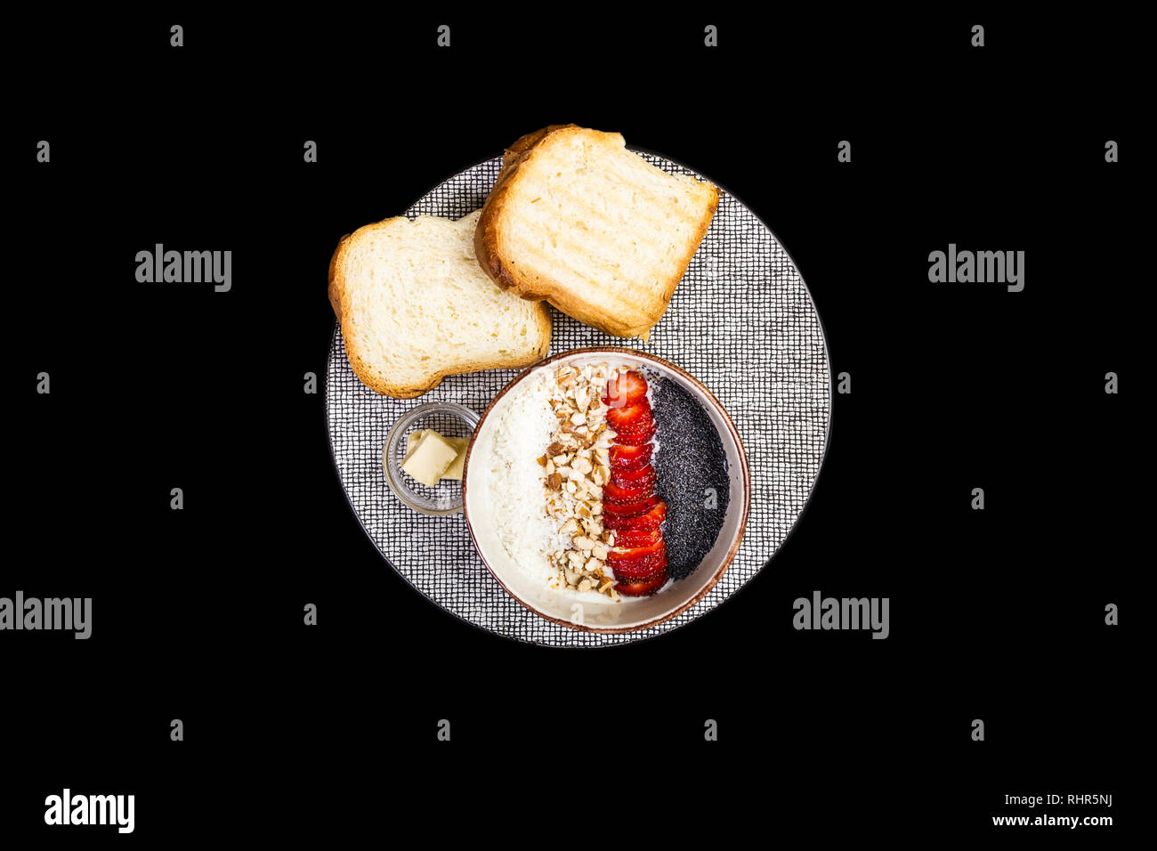Una sana prima colazione. Cereali di riso o porridge con fragole fresche, mandorla e scaglie di noce di cocco, servita con pane e burro. Isolato sul nero Foto Stock