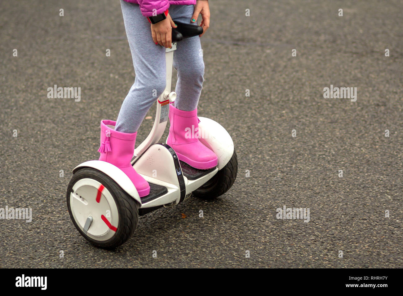 Close-up di bambino ragazza gambe in rosa luminoso stivali di gomma equitazione segway sulla soleggiata strada asfaltata spazio copia dello sfondo. La moderna tecnologia, bambini safet Foto Stock