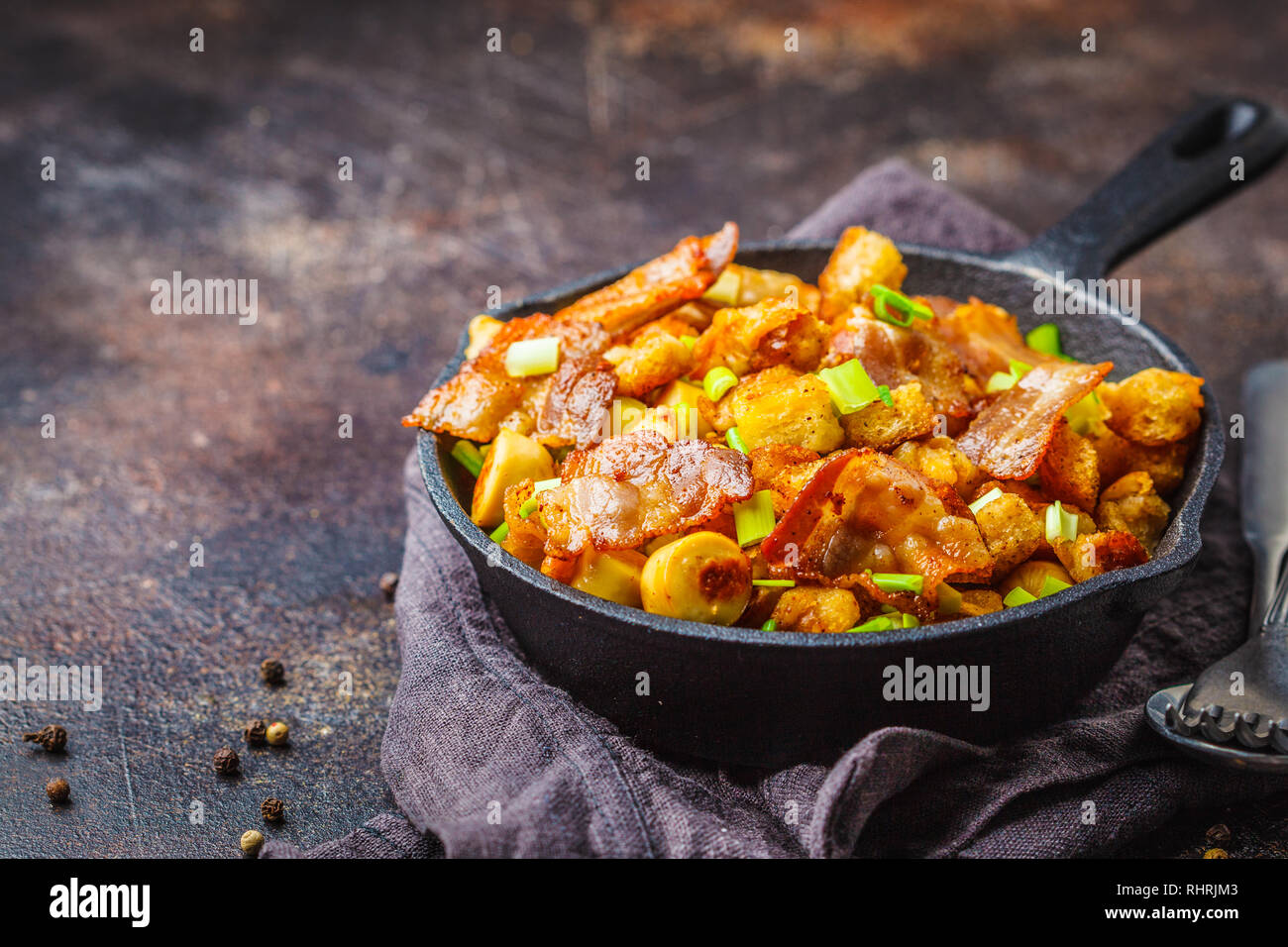 Lo spagnolo migas con carne di maiale e cipollotti in un cast-padella di ferro su uno sfondo scuro. Foto Stock