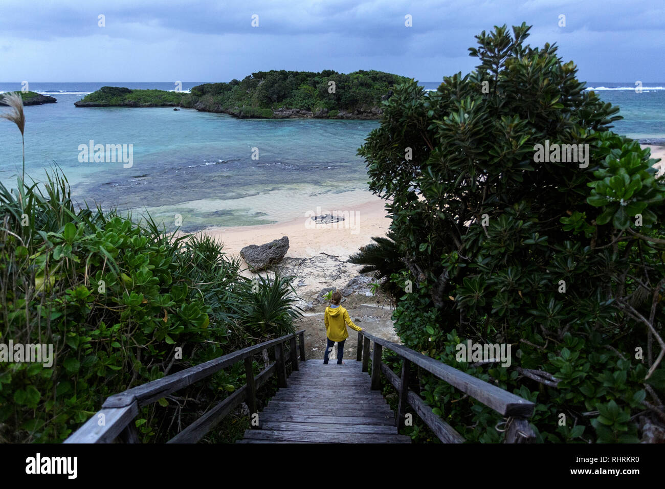 La donna in giallo Giacca pioggia permanente sulla passerella in legno per la bella sabbia spiaggia tropicale durante le tempeste, Giappone Foto Stock