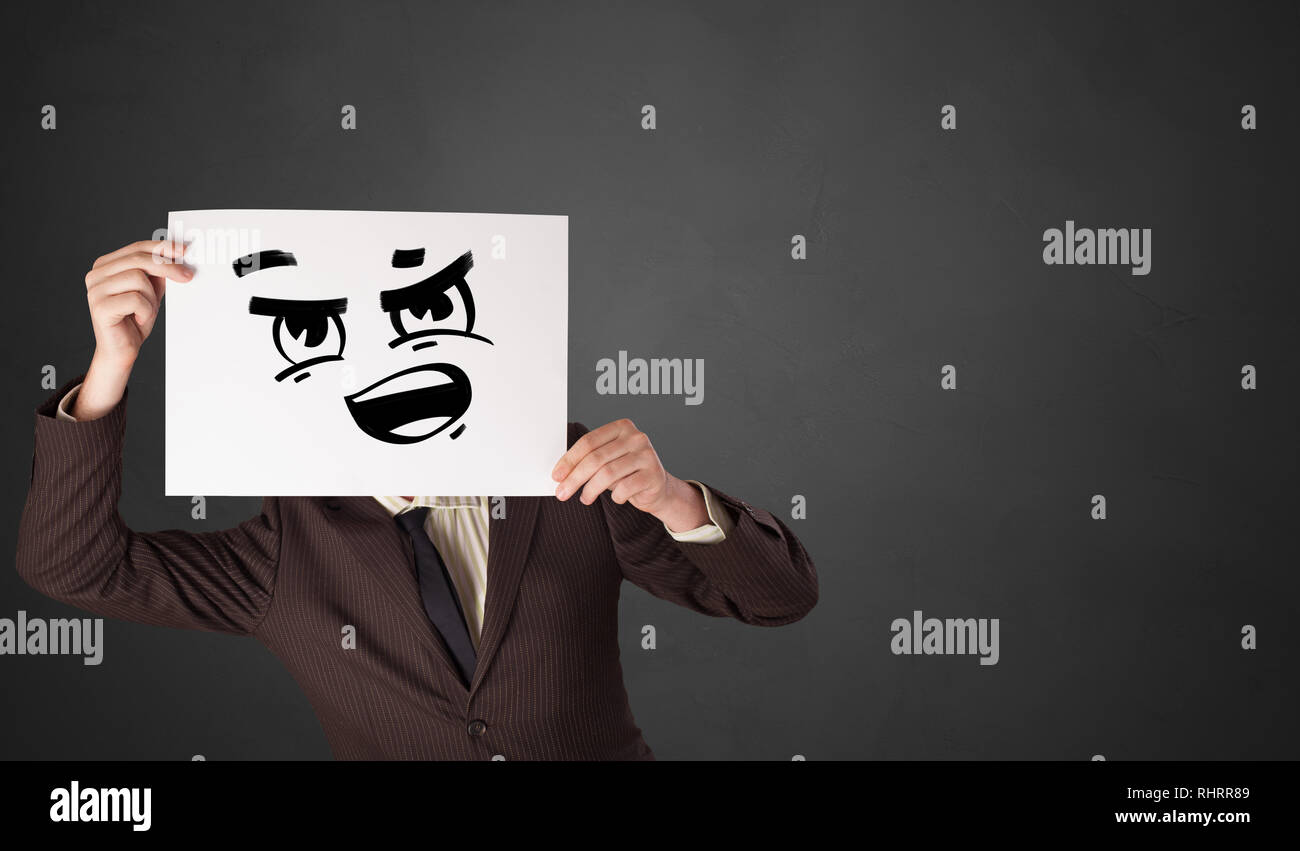 Casual persona in possesso di una carta con divertenti emoticon di fronte il suo volto Foto Stock