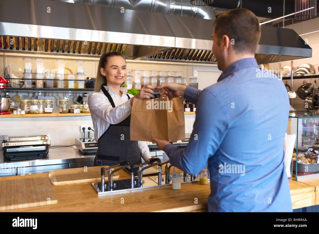 Sorridente giovane cameriera indossando il grembiule che serve cibo da asporto al cliente al bancone piccolo ristorante Foto Stock