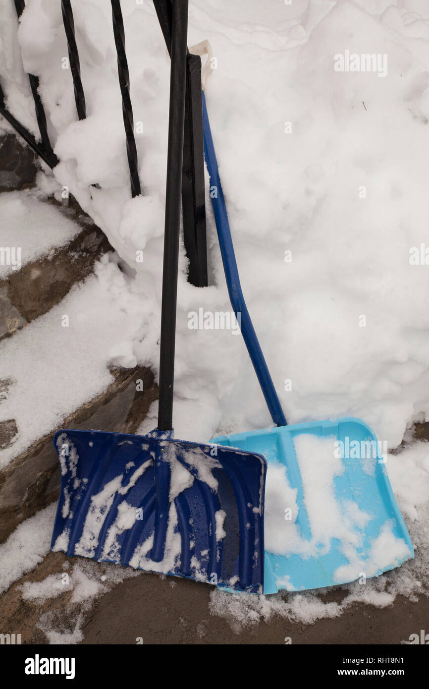 Due pale da neve appoggiarsi contro una cancellata in ferro battuto su una scalinata nevoso. Foto Stock