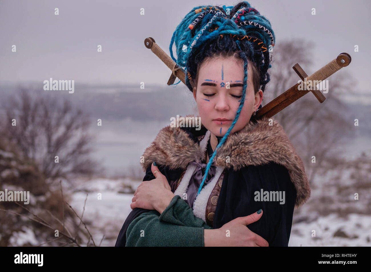 Malinconici Viking donna con una spada in un nero lungo mantello di pelliccia. ritratto di una ragazza sognante con gli occhi chiusi. Femmina con capelli blu dreadlocks e Foto Stock