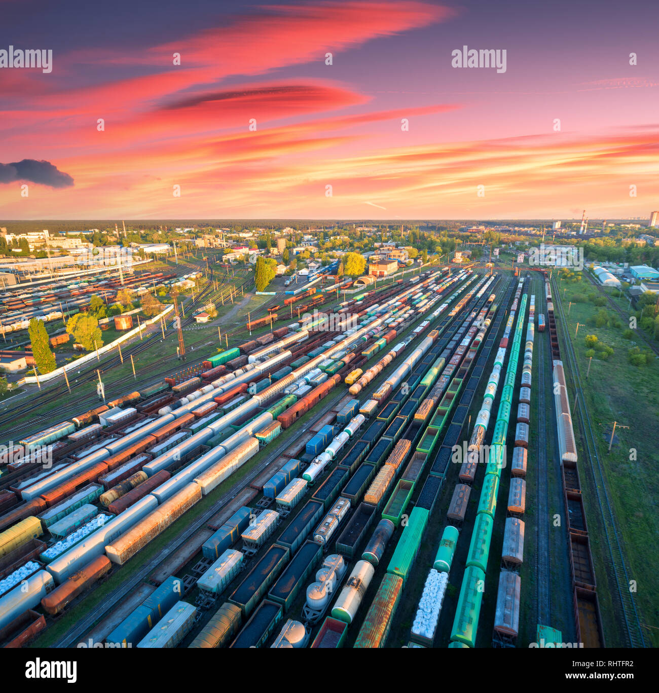 Vista aerea di treni merci sulla stazione ferroviaria al tramonto colorato. I carri con merci su ferrovia. Industria pesante. Industriali. I treni merci, città bui Foto Stock