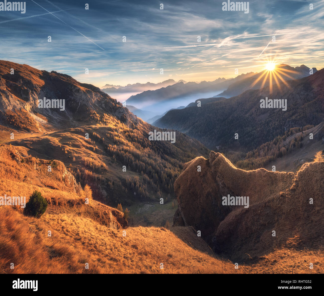 Montagne nella nebbia al bel tramonto in autunno. Dolomiti, Italia. Paesaggio alpino con mountain valley, arancione erba, nuvole basse, alberi sulle colline, blu Foto Stock