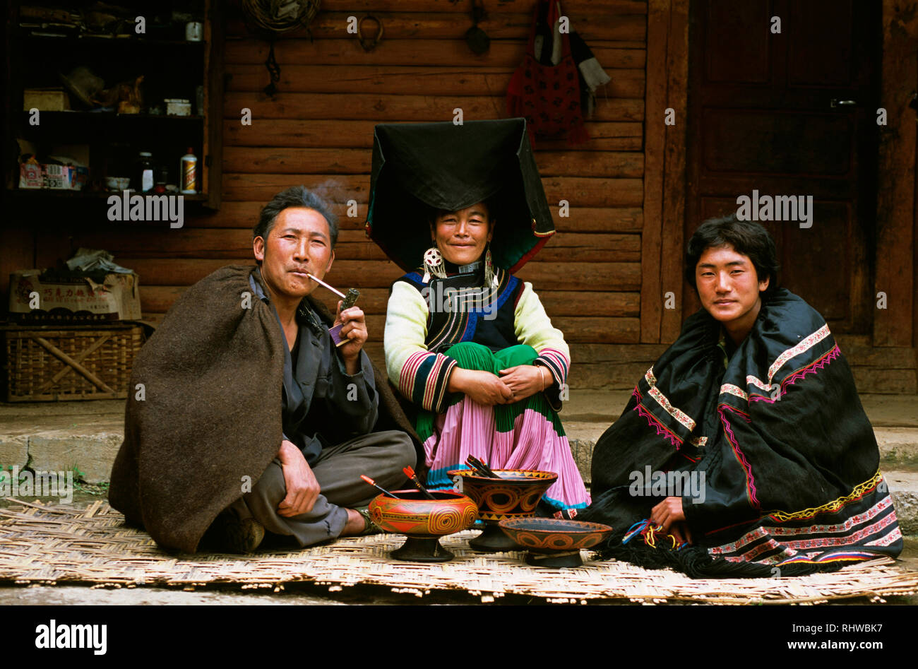 Un etnica Yi famiglia indossando vestiti tradizionali sedersi di fronte alla loro famiglia della collezione rara di bocce laccato in Yunnan in Cina. Foto Stock