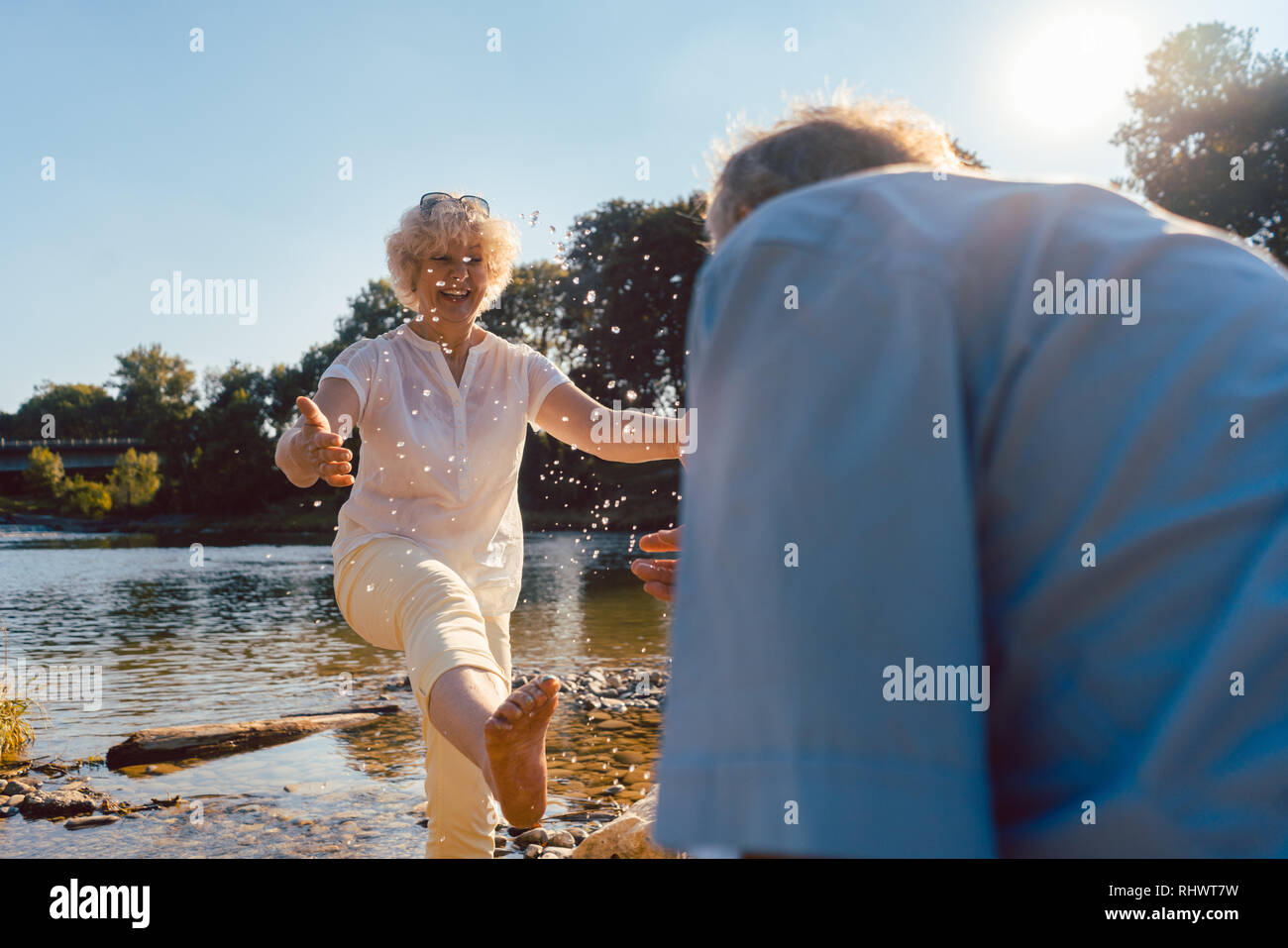 Divertente coppia senior giocando con acqua al fiume in una giornata di sole di estate Foto Stock