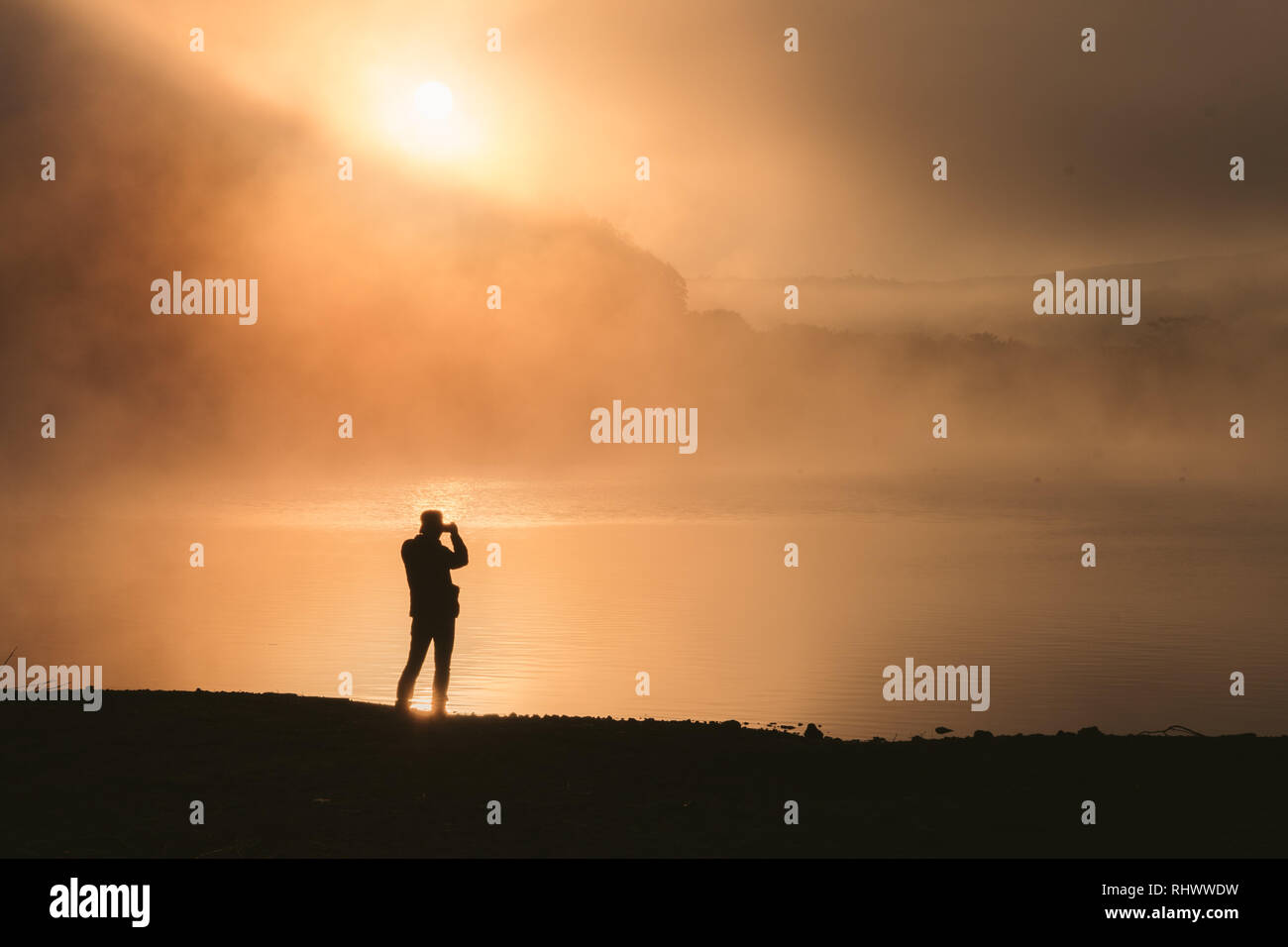 La sagoma di un uomo con un binocolo in una nebbiosa mattina presso il lago Shoji Foto Stock