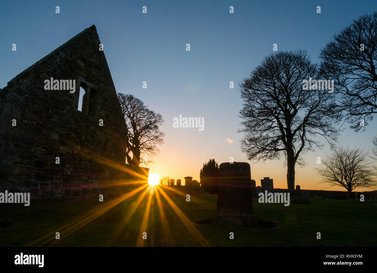 East Lothian, Scozia, Regno Unito, 4 febbraio 2019. Regno Unito: Meteo il sole irrompe attraverso sagome delle pareti in rovina di Gladsmuir vecchia chiesa parrocchiale e il cimitero con lapidi antiche al tramonto in inverno Foto Stock