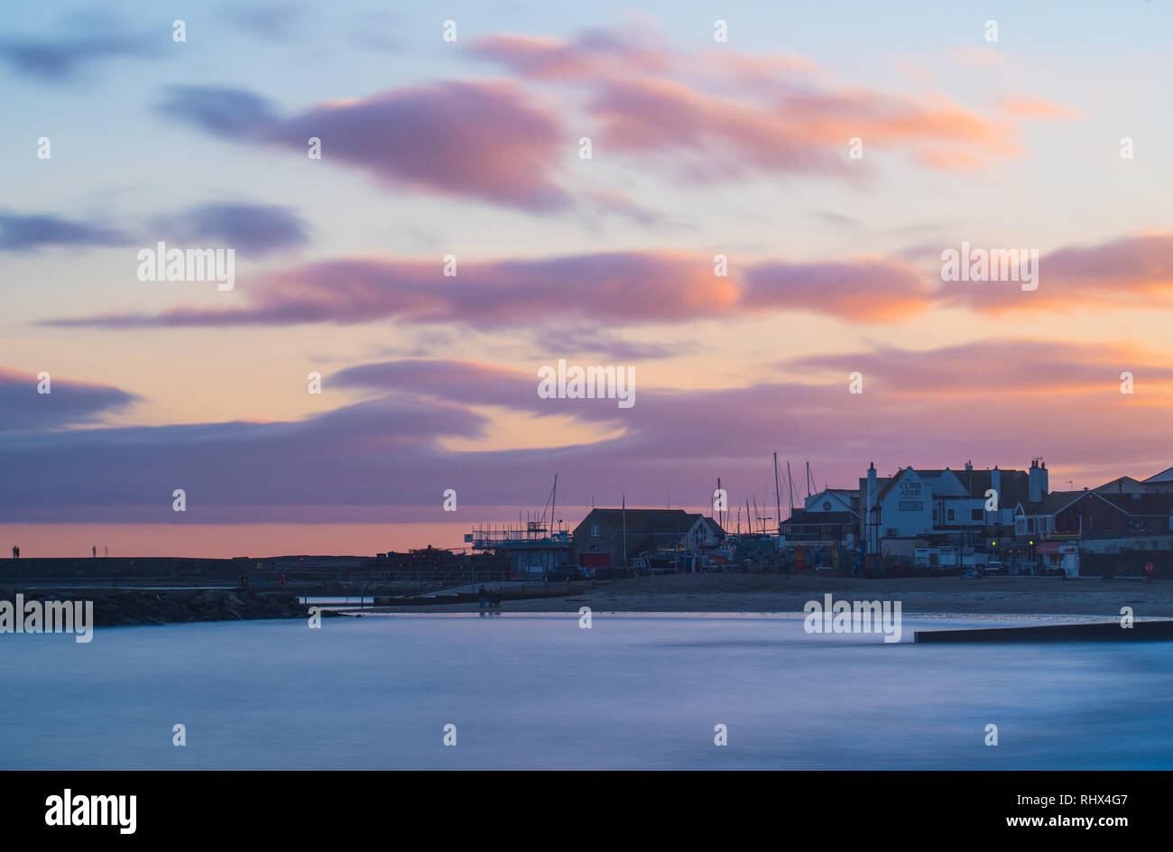 Lyme Regis, Dorset, Regno Unito. 4° febbraio 2019. Regno Unito: Meteo il cielo si illumina di arancione come il sole tramonta sul lungomare di edifici e il Cobb a Lyme Regis dopo una giornata di pioggia e forte vento. Credito: Celia McMahon/Alamy Live News Foto Stock