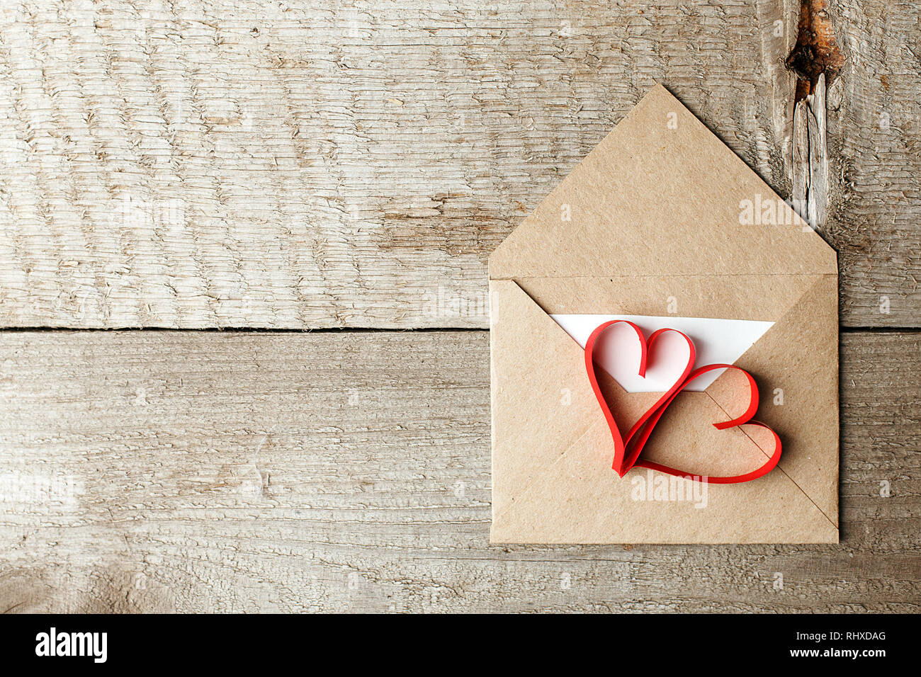 Lettera d'amore busta con cuori rossi su sfondo di legno, Valentino romanticismo closeup Foto Stock