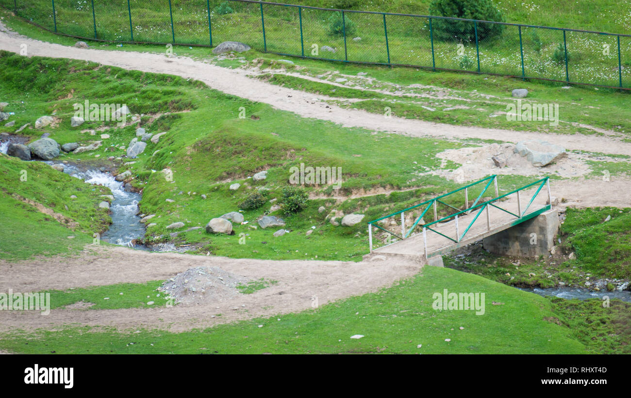 Un piccolo piede legno-ponte che attraversa un piccolo fiume in un lussureggiante verde prato in Pahalgam, Kashmir Foto Stock