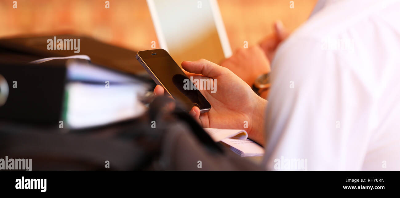 Close up dettaglio di un maschio di alta scuola studente utilizzando un telefono cellulare mentre studiava. Dettaglio sfocata del raccoglitore ad anelli cartella, penna, cancelleria e lapt Foto Stock