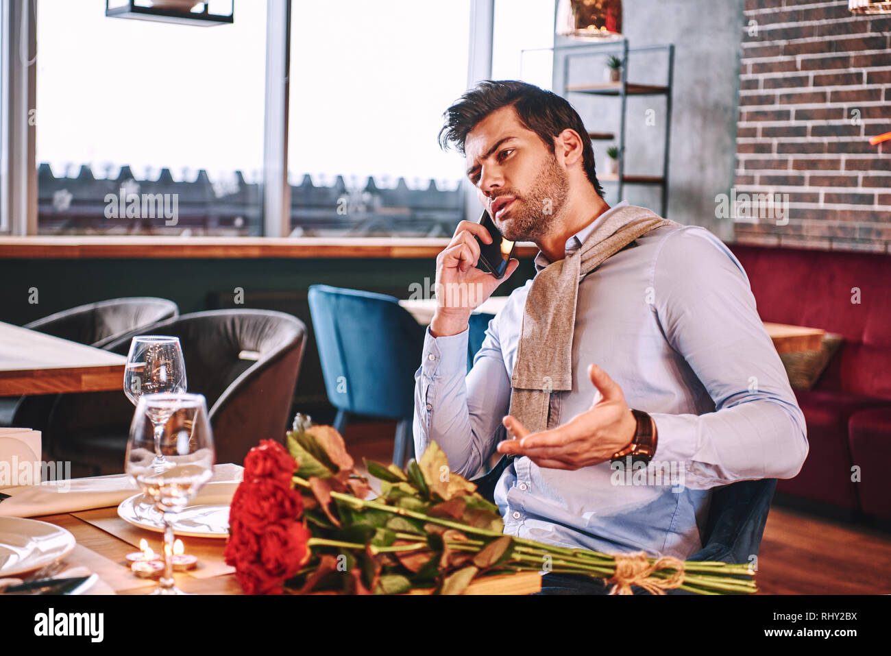 In attesa di fidanzata. L uomo è parlare tramite smartphone mentre si è in attesa nel ristorante la sua ragazza. Rose rosse sono sdraiato sul tavolo. Foto Stock