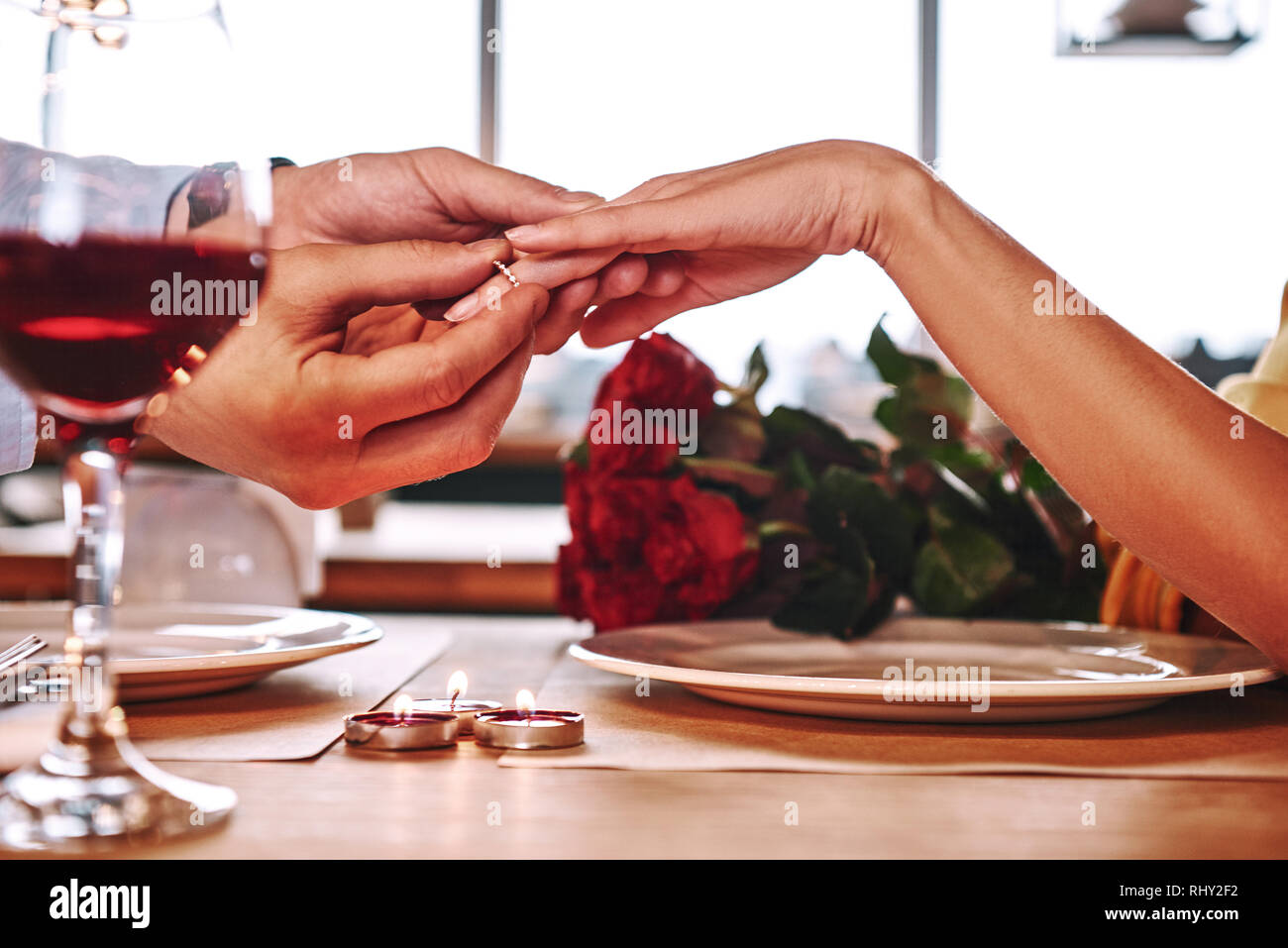 Proposta romantica. Giovane uomo anello di usura sulle mani della sua fidanzata nel ristorante. Rose rosse e candele sono giacenti sul tavolo vicino al vino rosso. Foto Stock