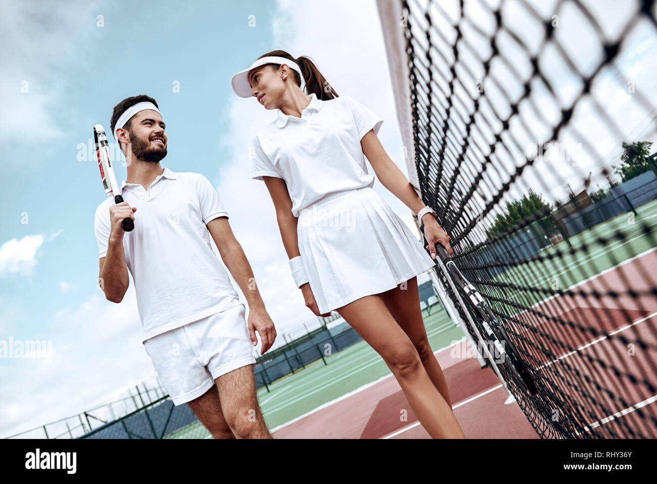 Gli amanti in bianco per abbigliamento sportivo con le racchette nelle loro mani guardare a ogni altro mentre andando a giocare a tennis su corte Foto Stock