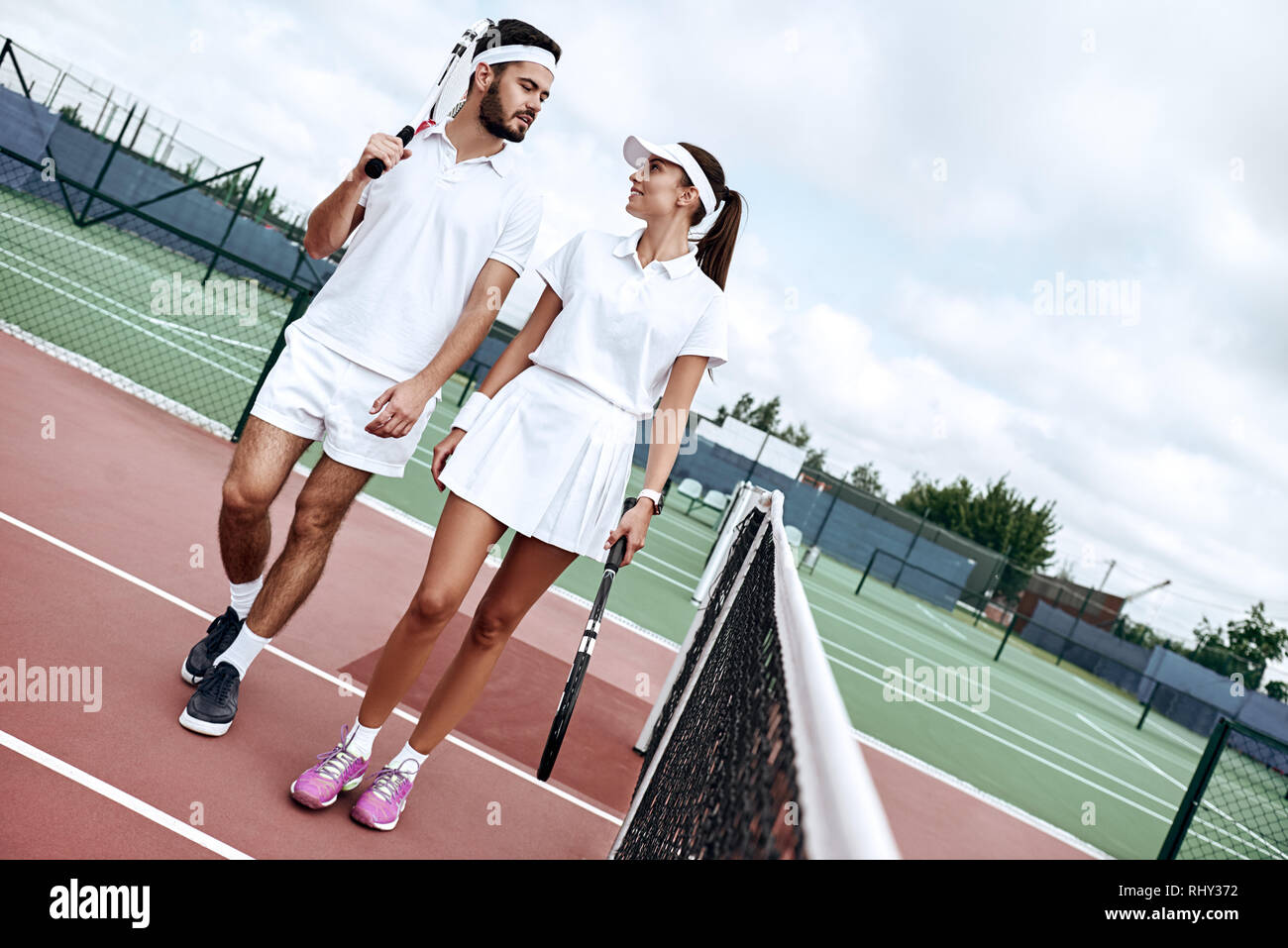 Gli amanti in bianco per abbigliamento sportivo con le racchette nelle loro mani guardare a ogni altro mentre andando a giocare a tennis su corte Foto Stock