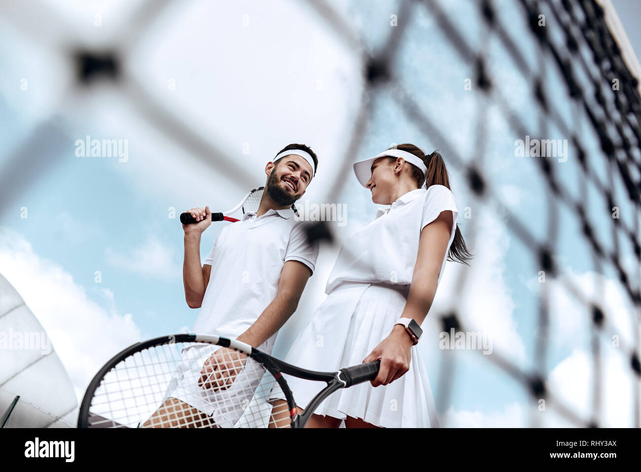 Gli amanti in bianco per abbigliamento sportivo con le racchette nelle loro mani trascorrere del tempo insieme giocando a tennis su corte Foto Stock