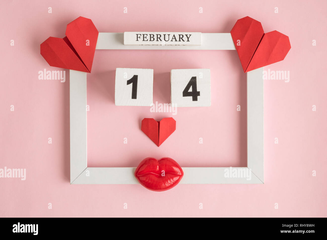 Piatto di laici photo frame con cuori origami, calendario di legno e plastica labbra contro di rosa pastello minima di sfondo il giorno di San Valentino del concetto. Foto Stock