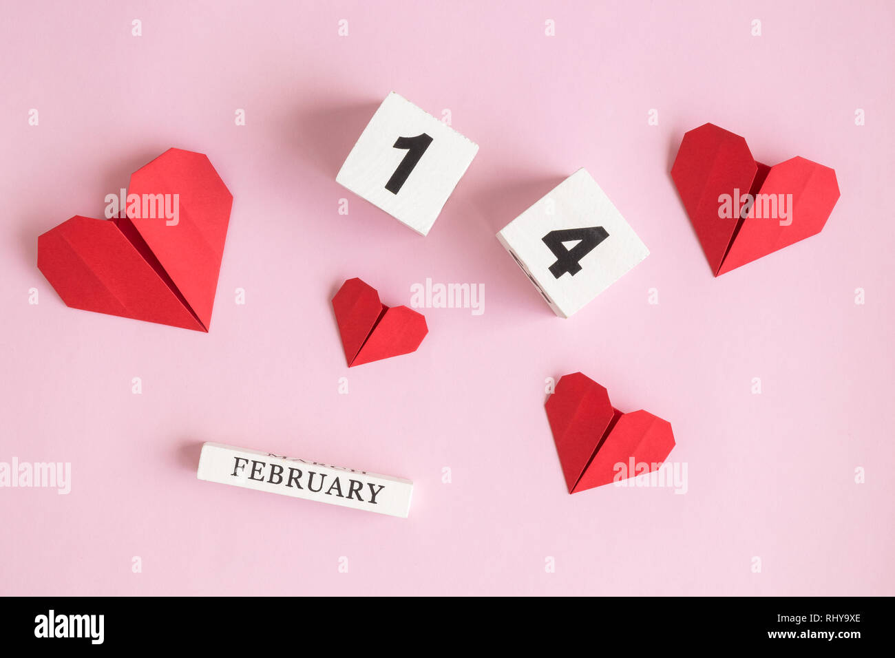 Piatto di laici calendario di legno e di carta origami cuori contro di rosa pastello minima di sfondo il giorno di San Valentino del concetto. Foto Stock