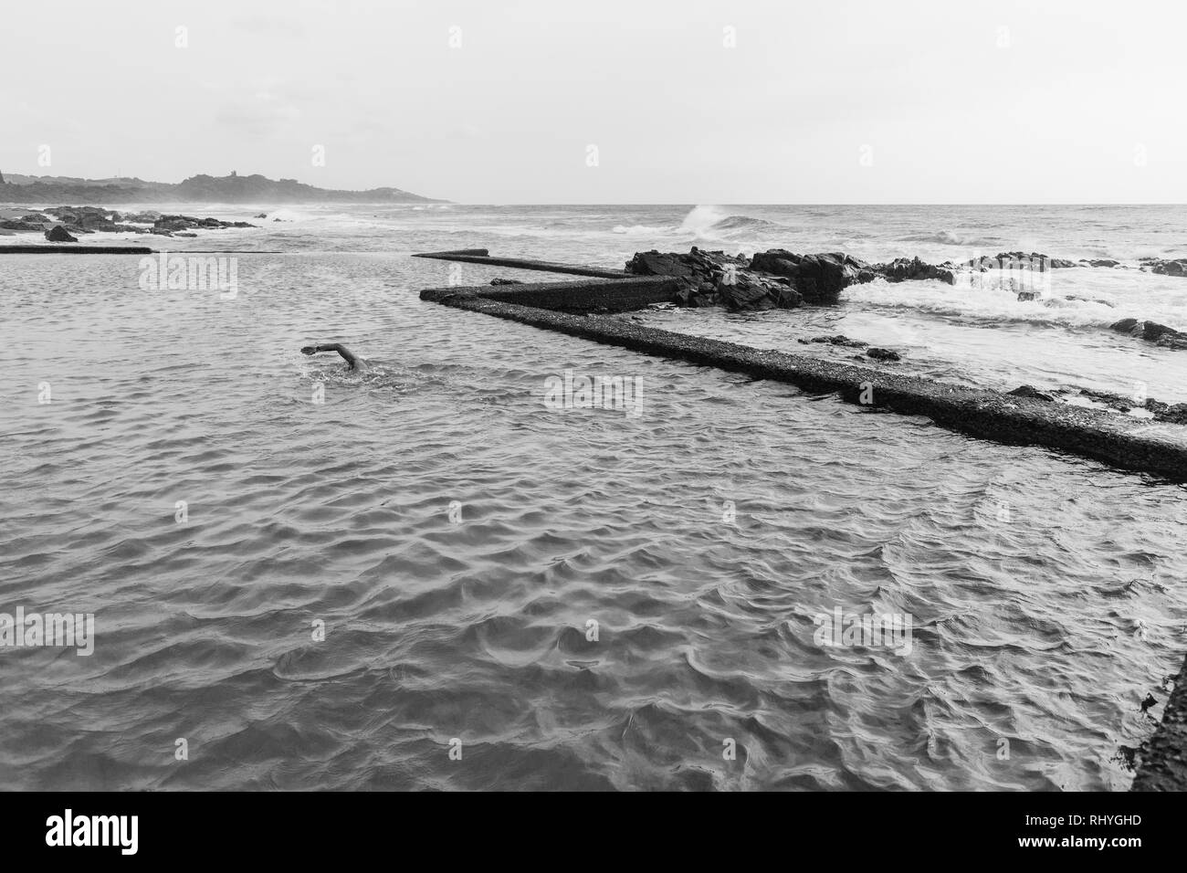 Maschio dedicato nuoto fitness esercizio in beach ocean pool di marea ventoso contrastato condizioni in foto in bianco e nero. Foto Stock