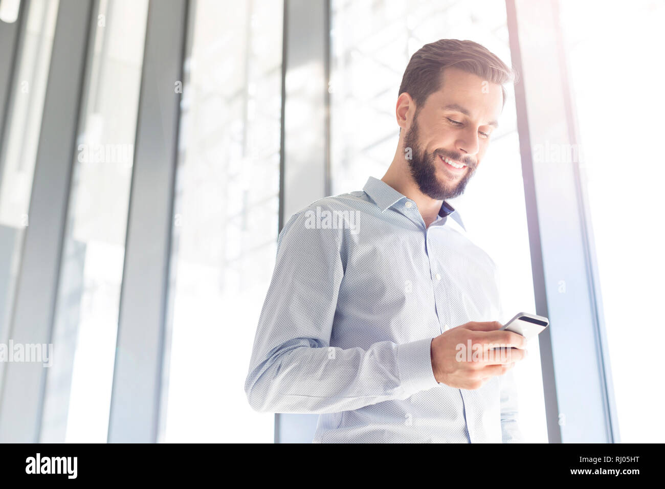 Imprenditore sorridente sms sul cellulare in ufficio Foto Stock
