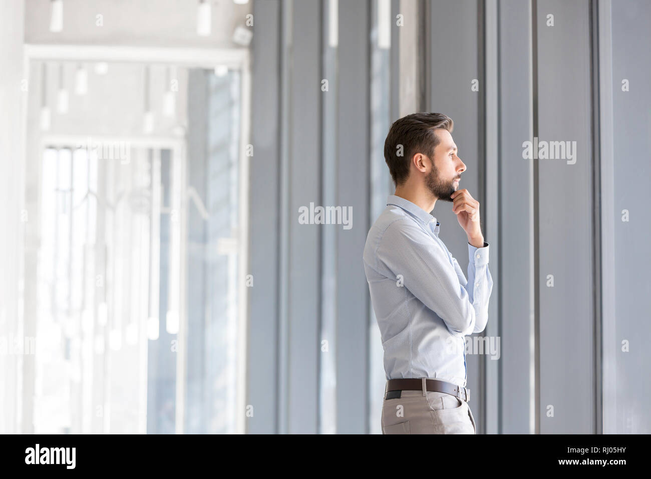 Vista laterale di pensosa imprenditore in piedi in ufficio Foto Stock