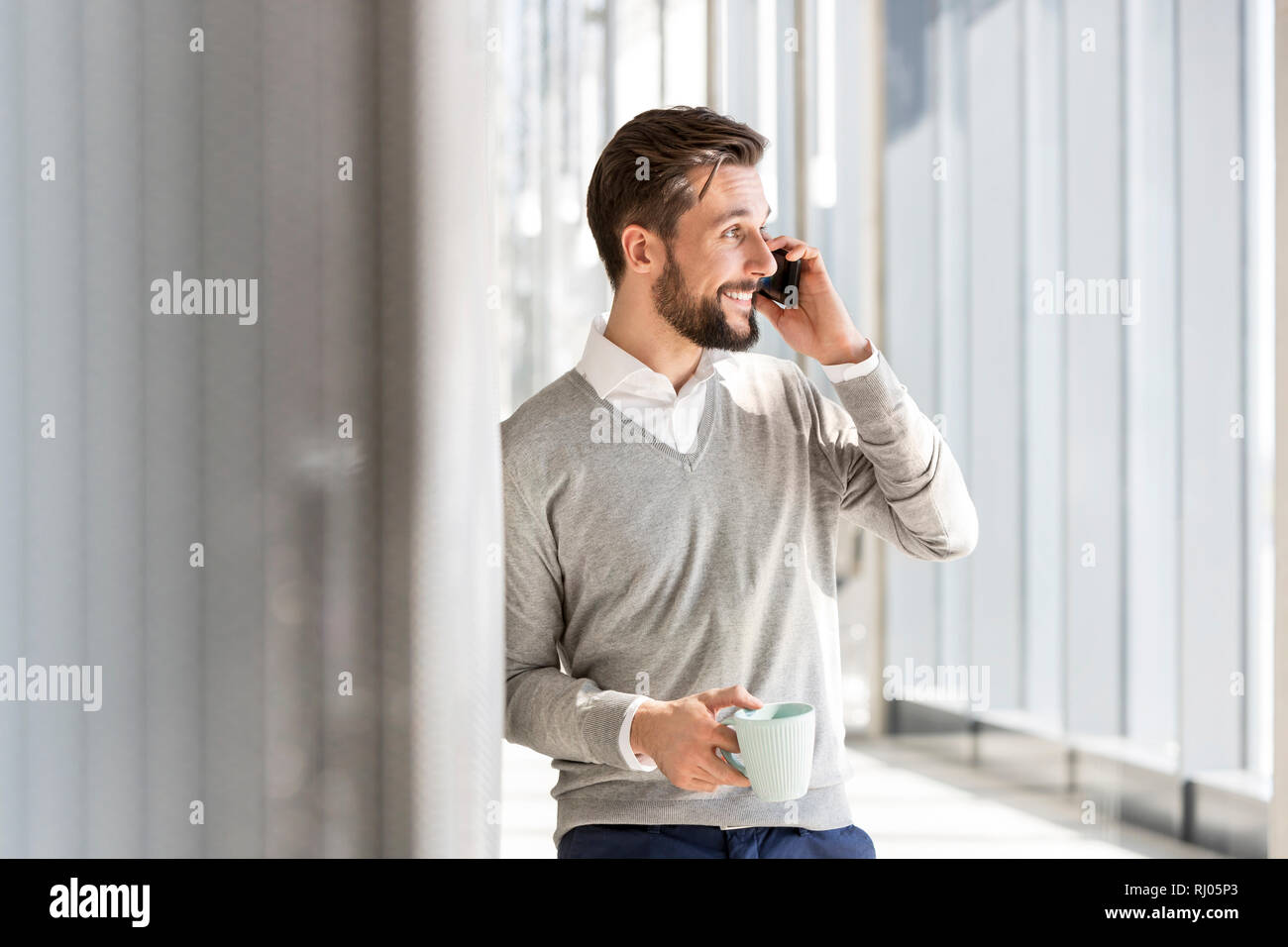 Imprenditore sorridente parlando al telefono cellulare mentre un caffè in ufficio Foto Stock