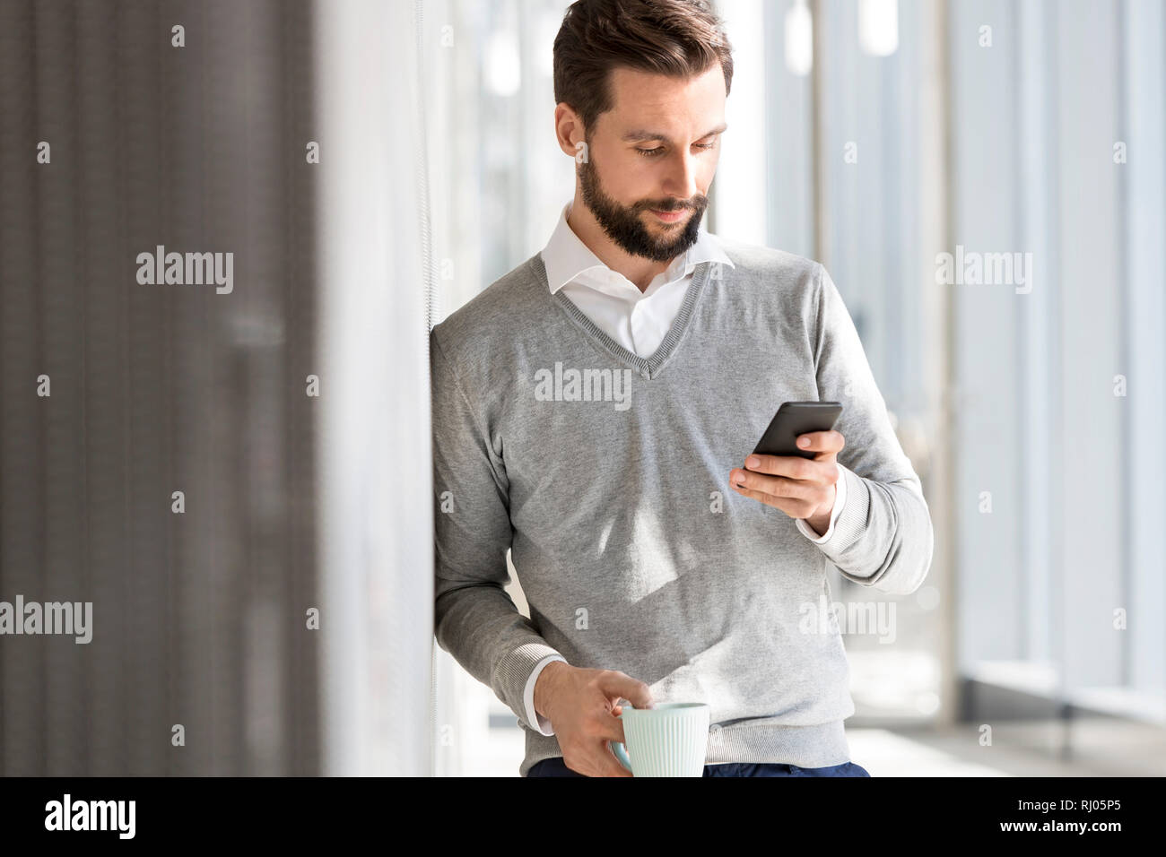 Imprenditore sms sul cellulare mentre un caffè in ufficio Foto Stock