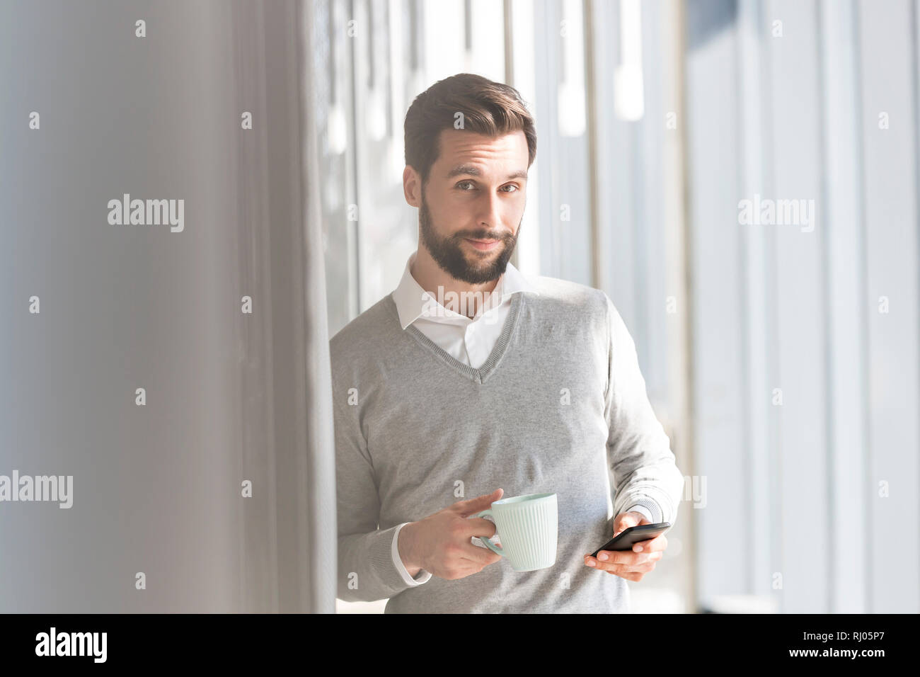 Ritratto di imprenditore sorridente con telefono cellulare avente il caffè in ufficio Foto Stock