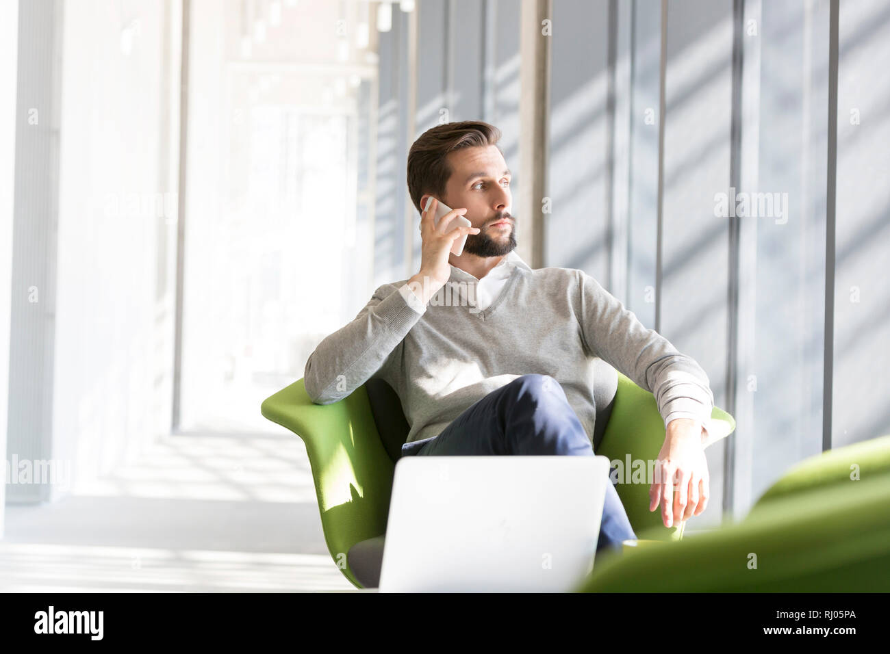 Imprenditore parlando al telefono cellulare mentre è seduto su una sedia in ufficio Foto Stock