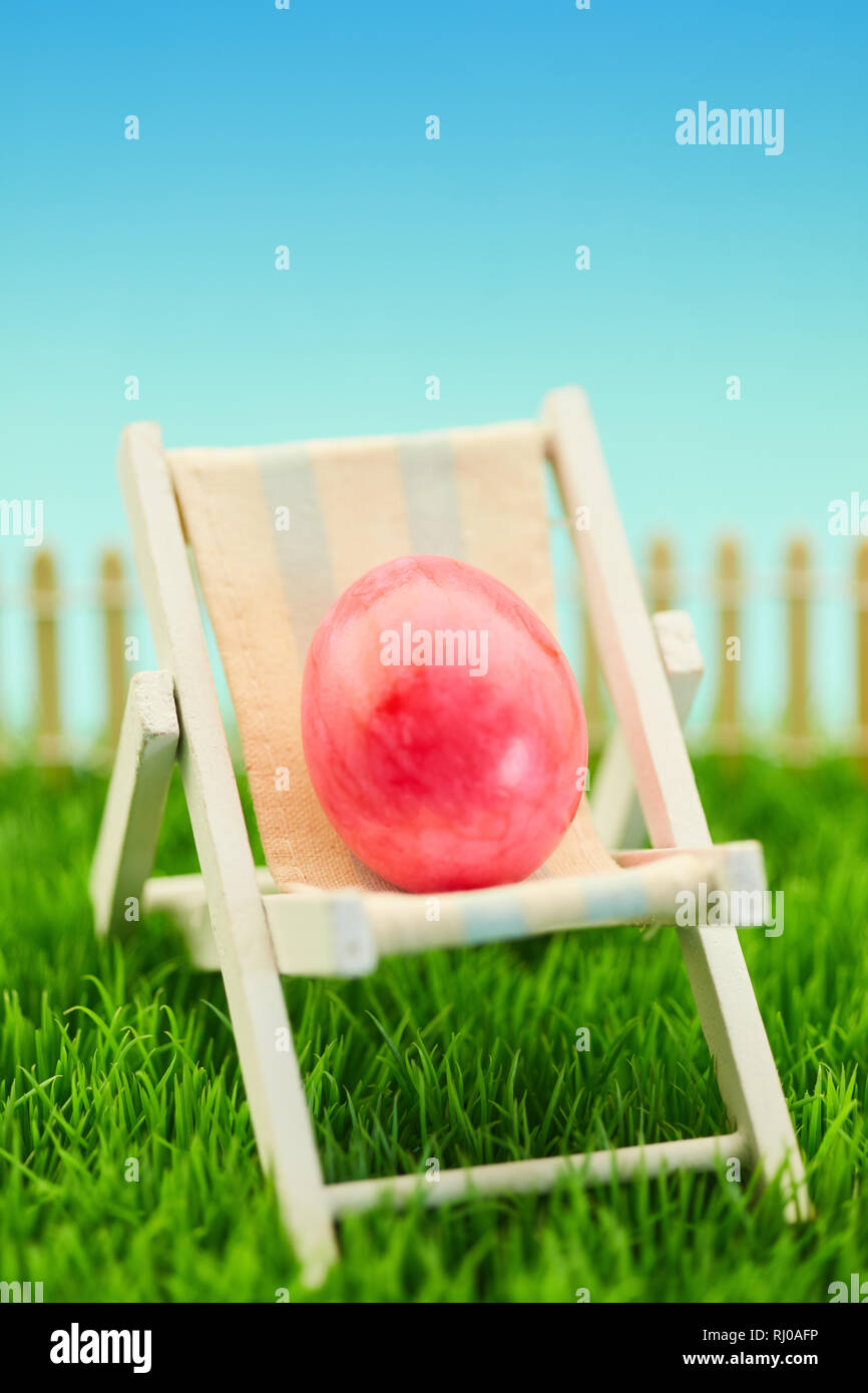 Uovo di Pasqua nella struttura di poltrona sdraio come le vacanze di Pasqua. Concetto su un verde prato Foto Stock