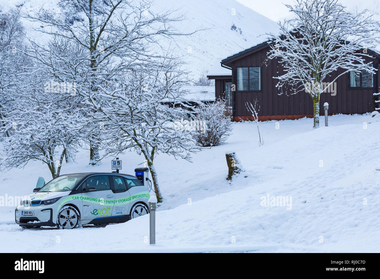 BMW auto elettrica essendo caricato in auto elettrica stazione di ricarica punto nella neve parcheggio coperto da Clachaig Inn, Glencoe, altopiani, Scozia in inverno Foto Stock