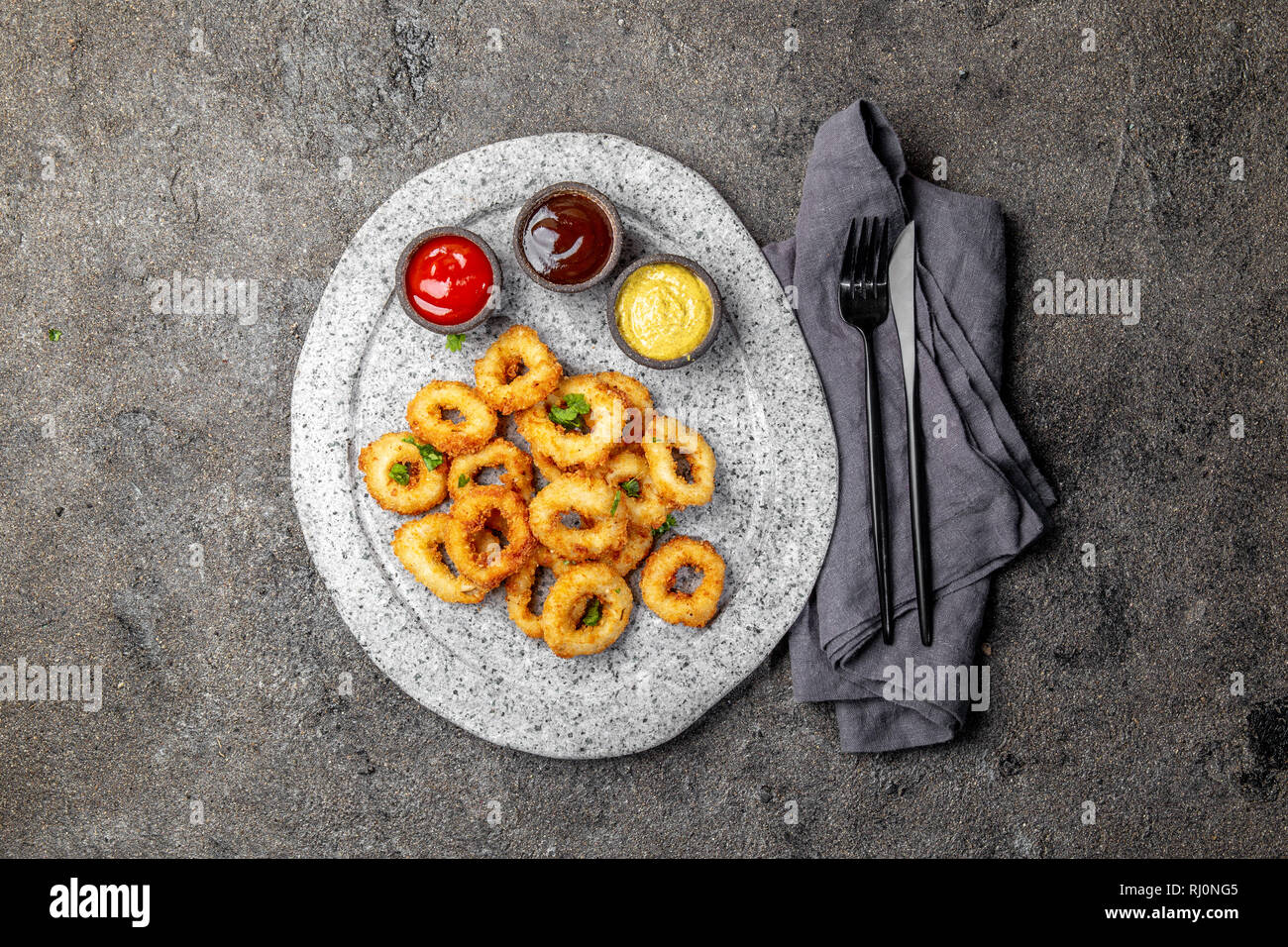 Calamari fritti anelli in pietra grigia piastra con salse. Grigio sfondo concreto Foto Stock